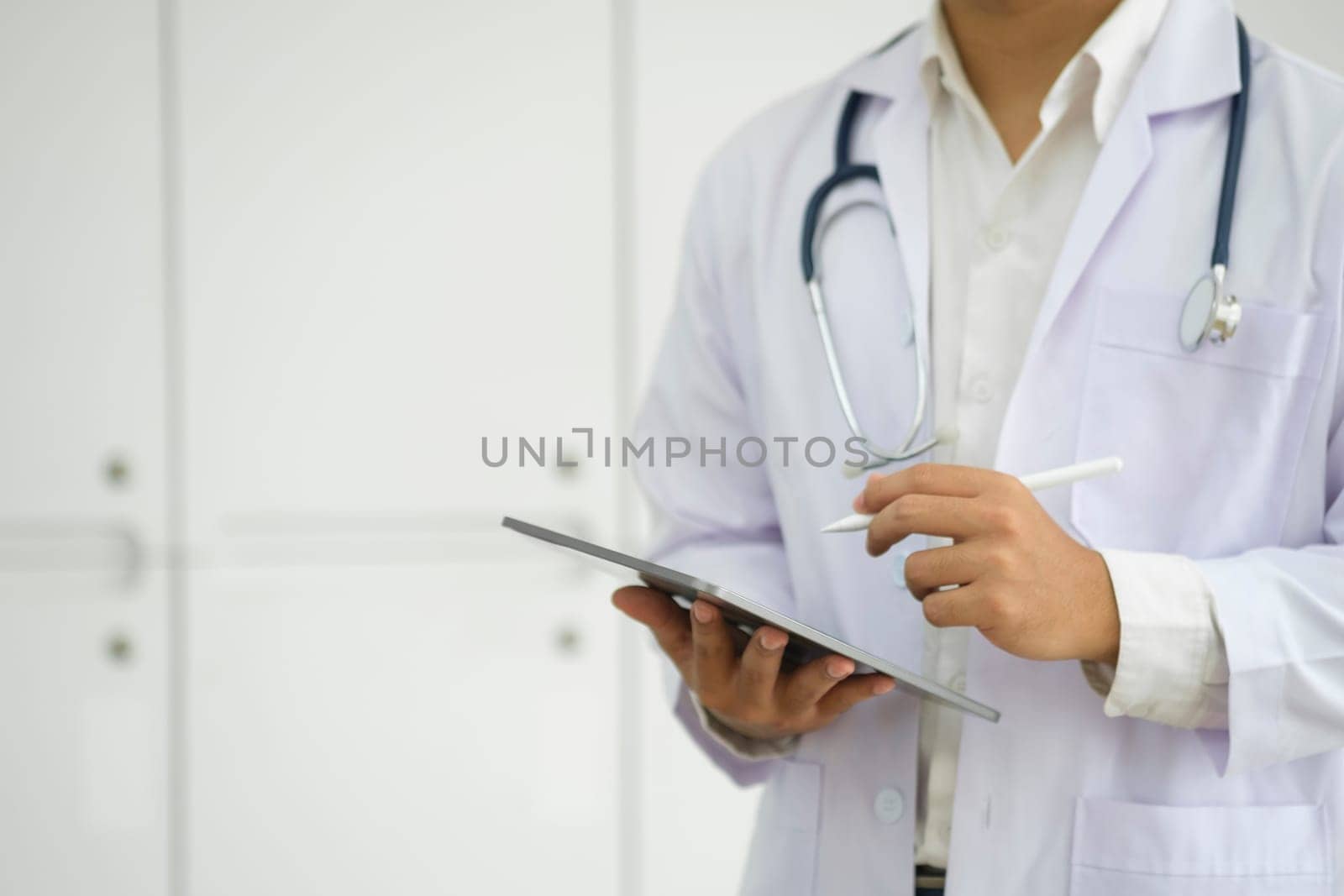 Cropped shot of a doctor using a digital tablet. Close up of doctor hands using digital tablet at clinic. Closeup of doctor in labcoat and stethoscope holding digital tablet. Doctor working on a tablet..