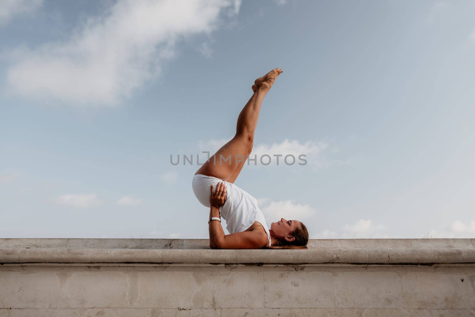 Fitness woman sea. A happy middle aged woman in white sportswear exercises morning outdoors in a park with a beach view. Female fitness pilates yoga routine concept. Healthy lifestyle. by panophotograph