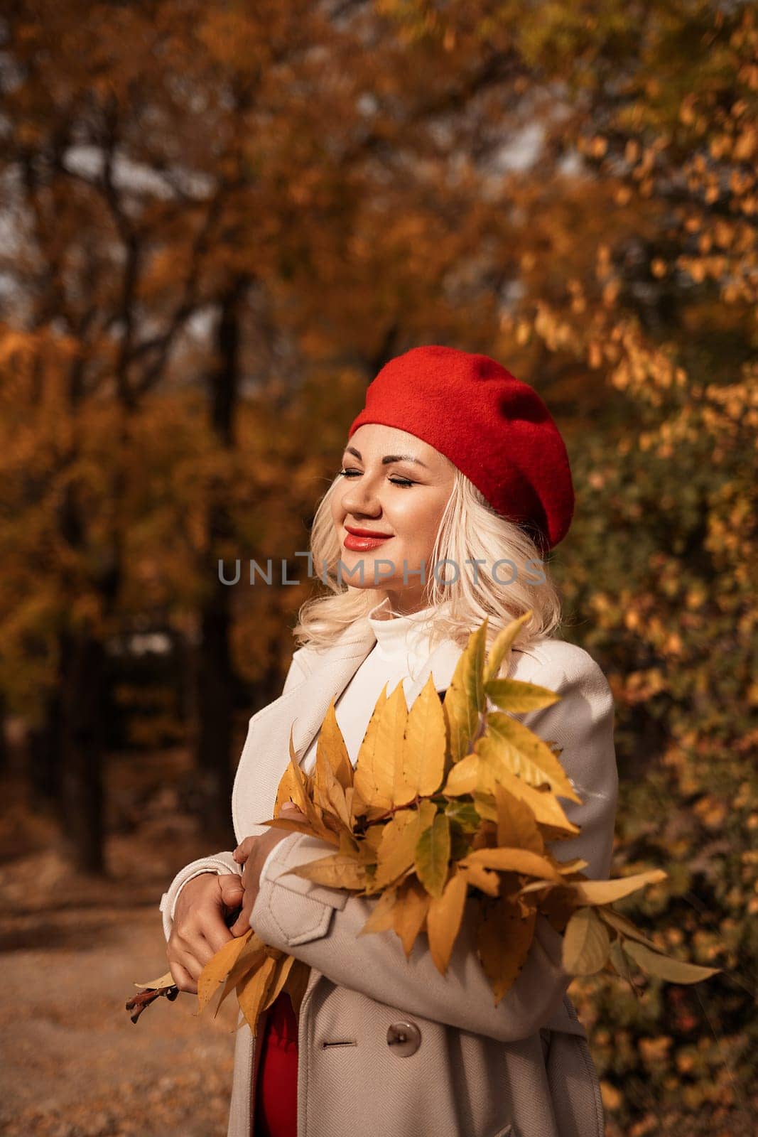 autumn woman in a red beret, a light coat and a red skirt, against the backdrop of an autumn park with yellow leaves in her hands by Matiunina