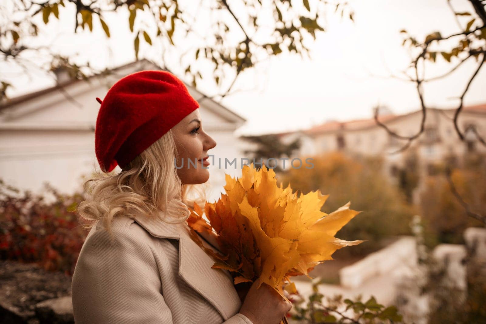 autumn woman in a red beret, a light coat and a red skirt, against the backdrop of an autumn park with yellow leaves in her hands by Matiunina