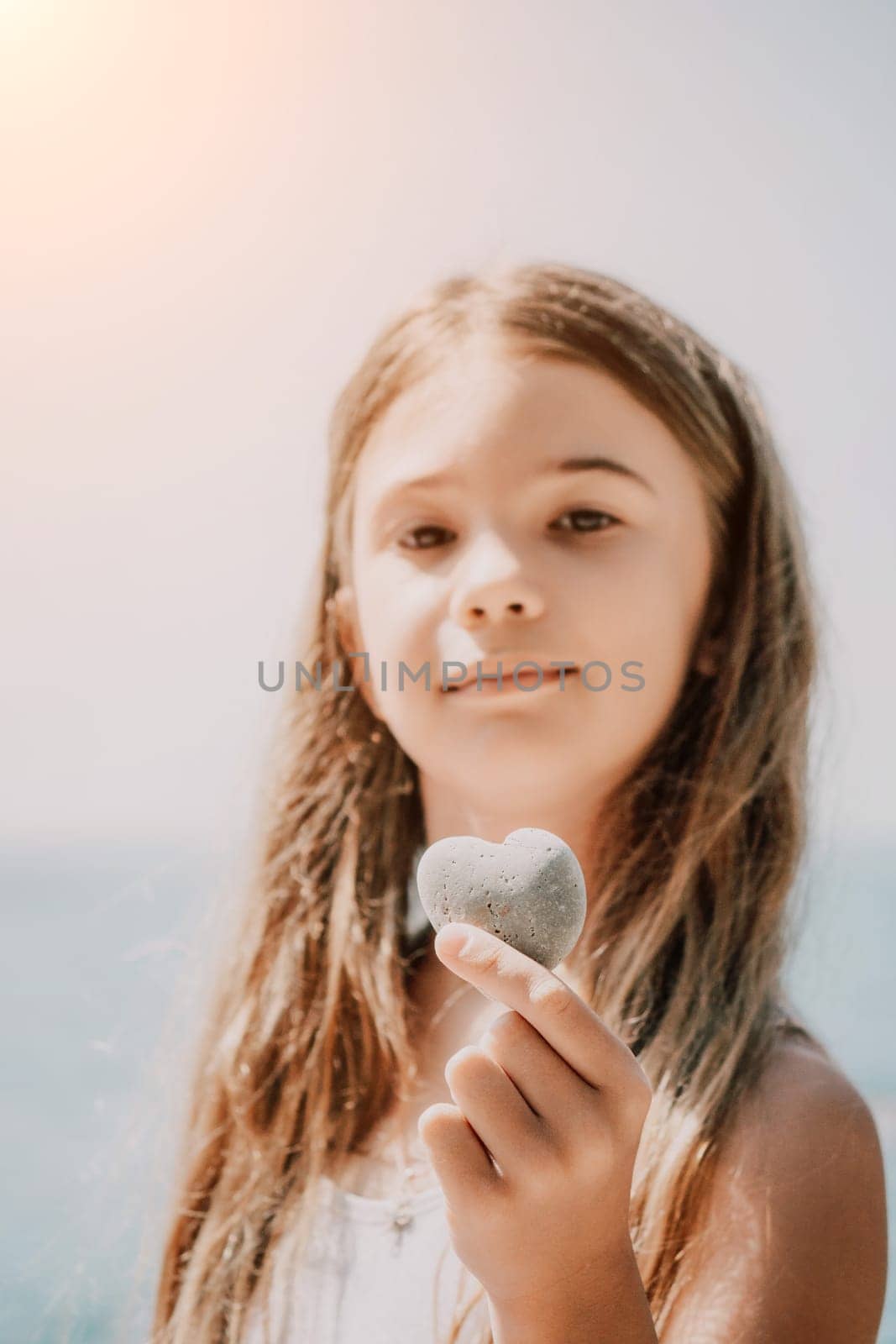 Happy girl holding in hand a stone in the shape of a heart against the background of the sea. Summer holiday vacation and travel concept. by panophotograph