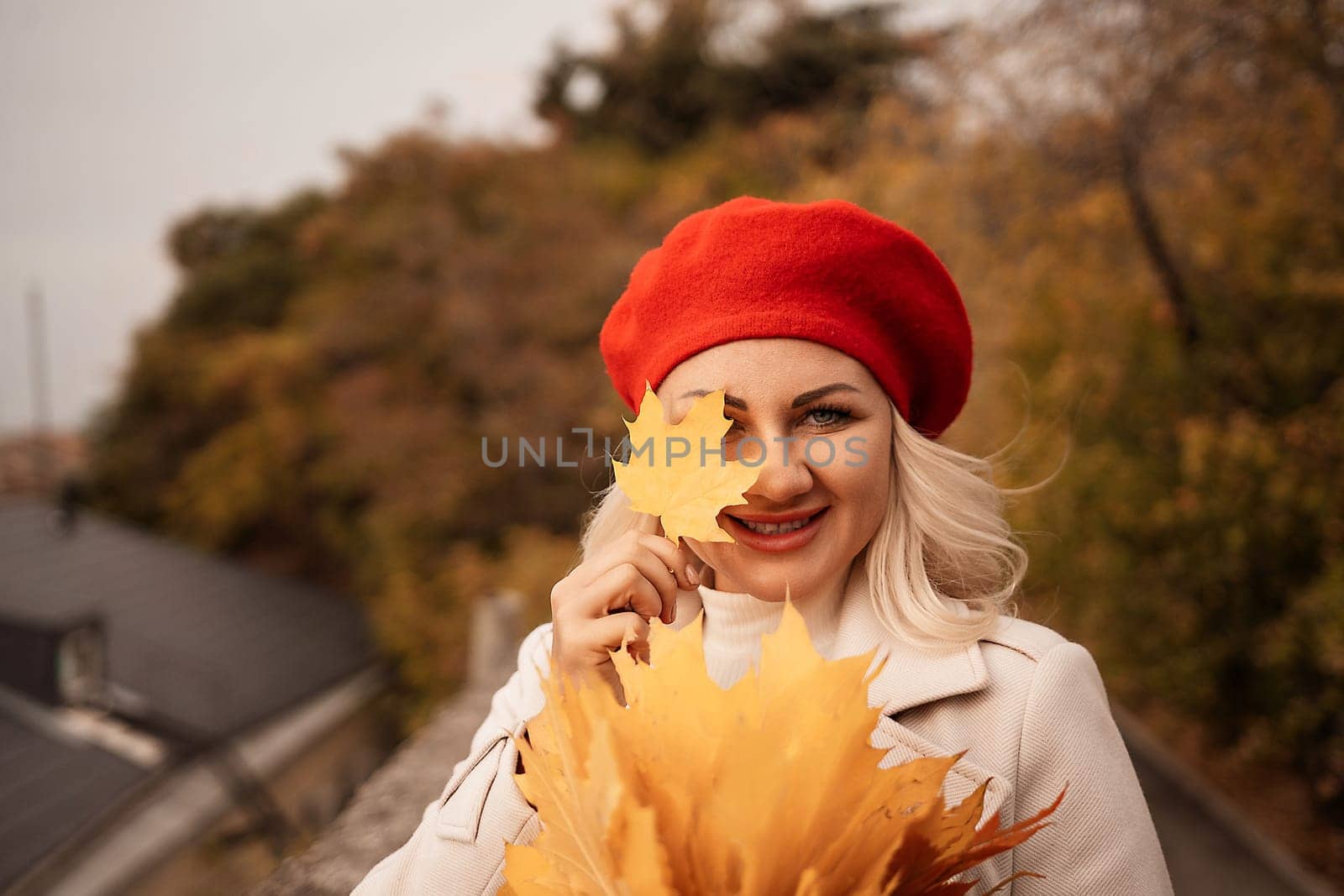 autumn woman in a red beret, a light coat and a red skirt, against the backdrop of an autumn park with yellow leaves in her hands by Matiunina