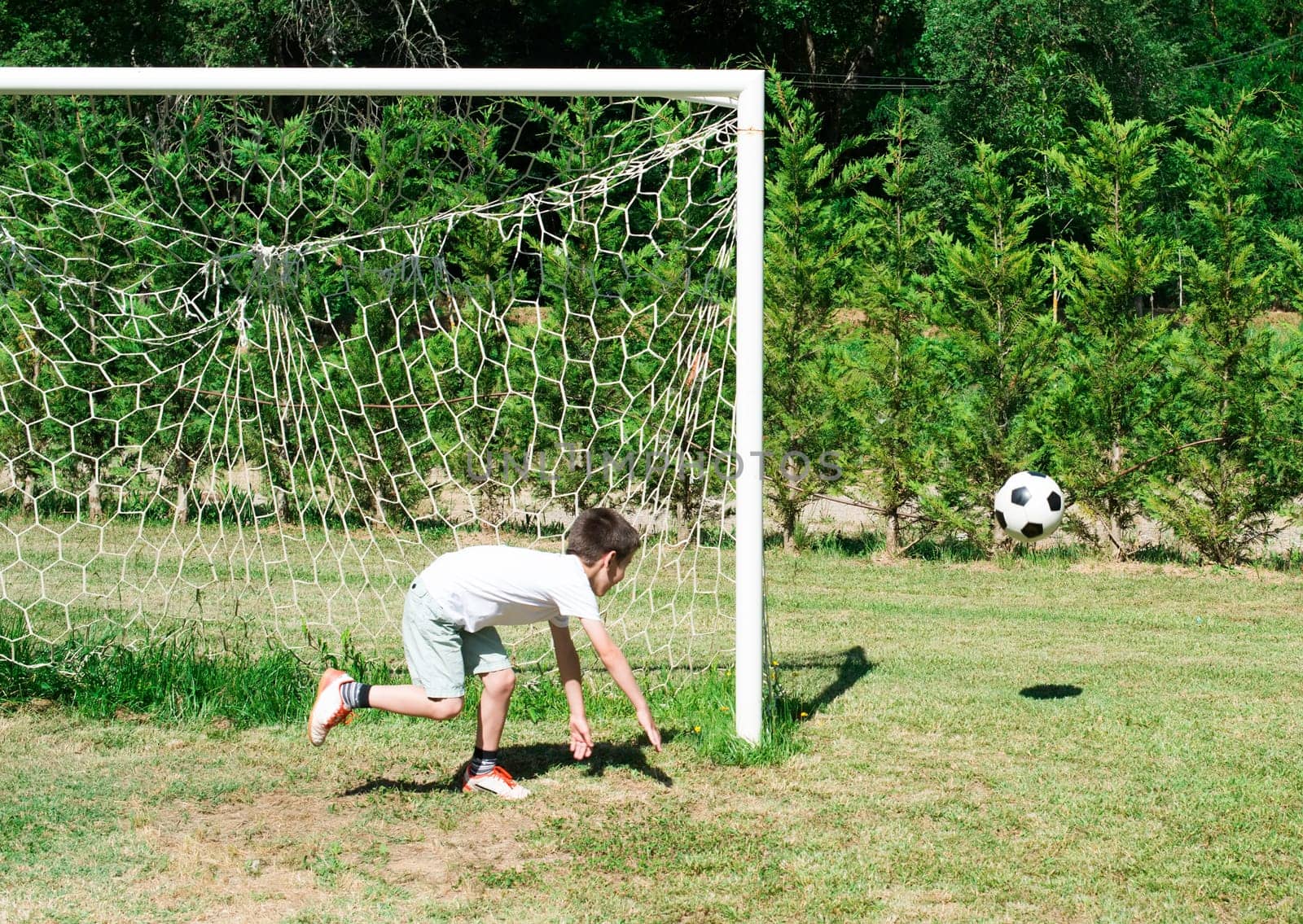 Child playing football in a stadium. Trees on the background