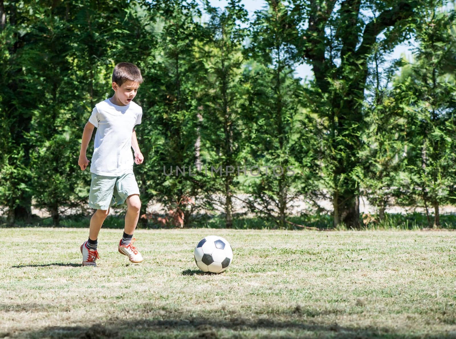 Child playing football in a stadium. Trees on the background