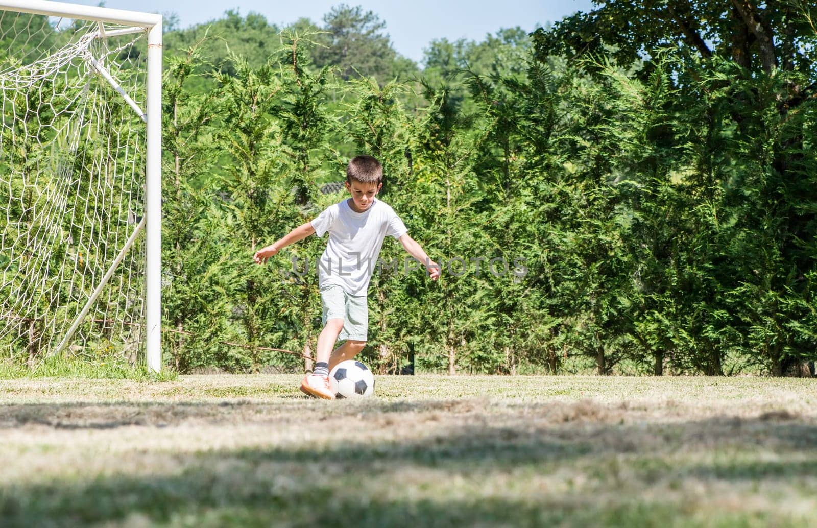 Child playing football in a stadium. Trees on the background
