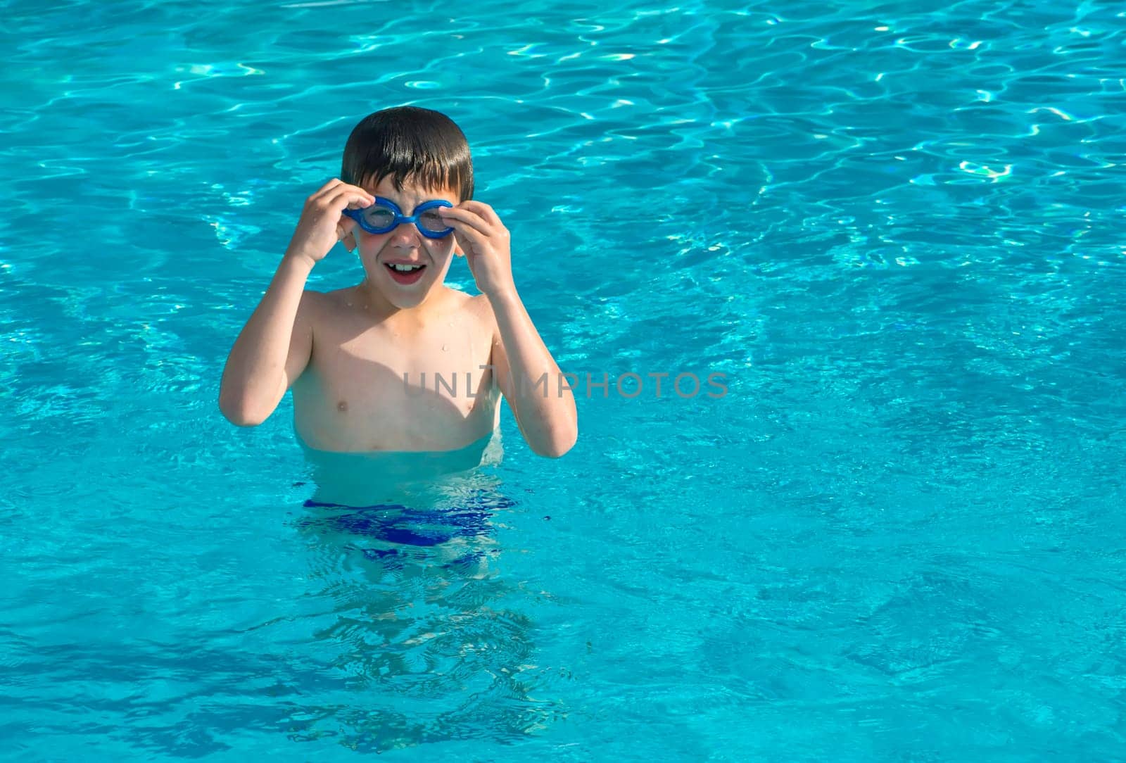 Child in swiming pool. Blue glasses