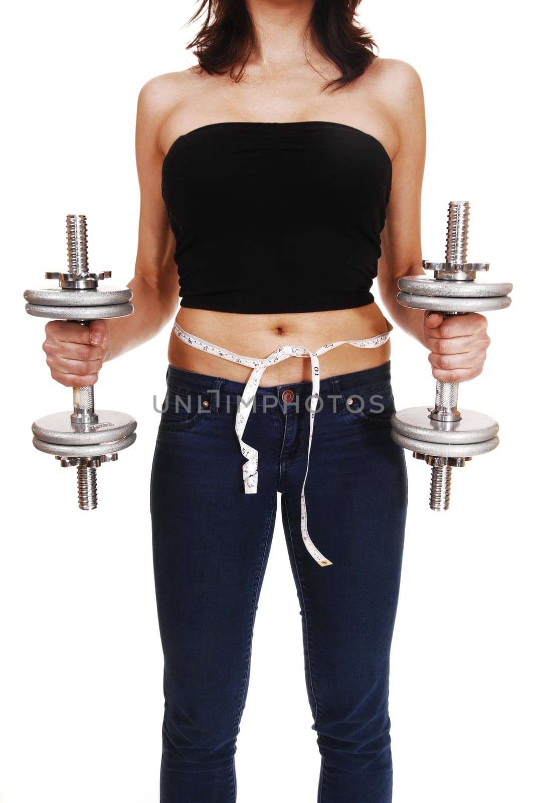 A closeup picture of the front section of a young woman in jeans, holding.two dumbbell's and a tape around her body, isolated on white background..