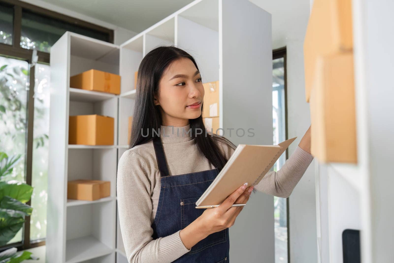A young woman efficiently organizes inventory and manages packages in a bright workspace, showcasing her attention to detail.