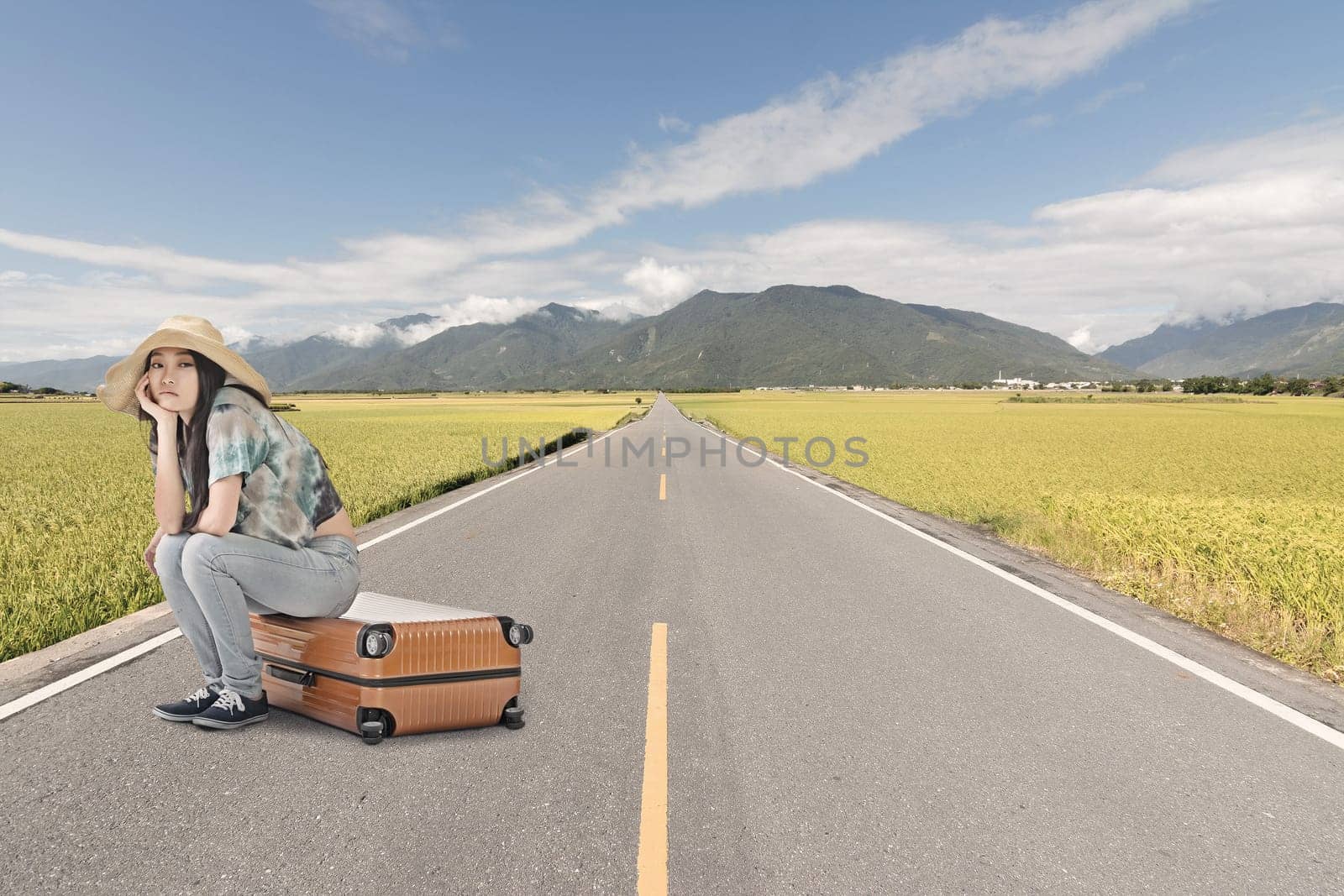 Asian woman thinking and sitting on a luggage on the ground of road in countryside.