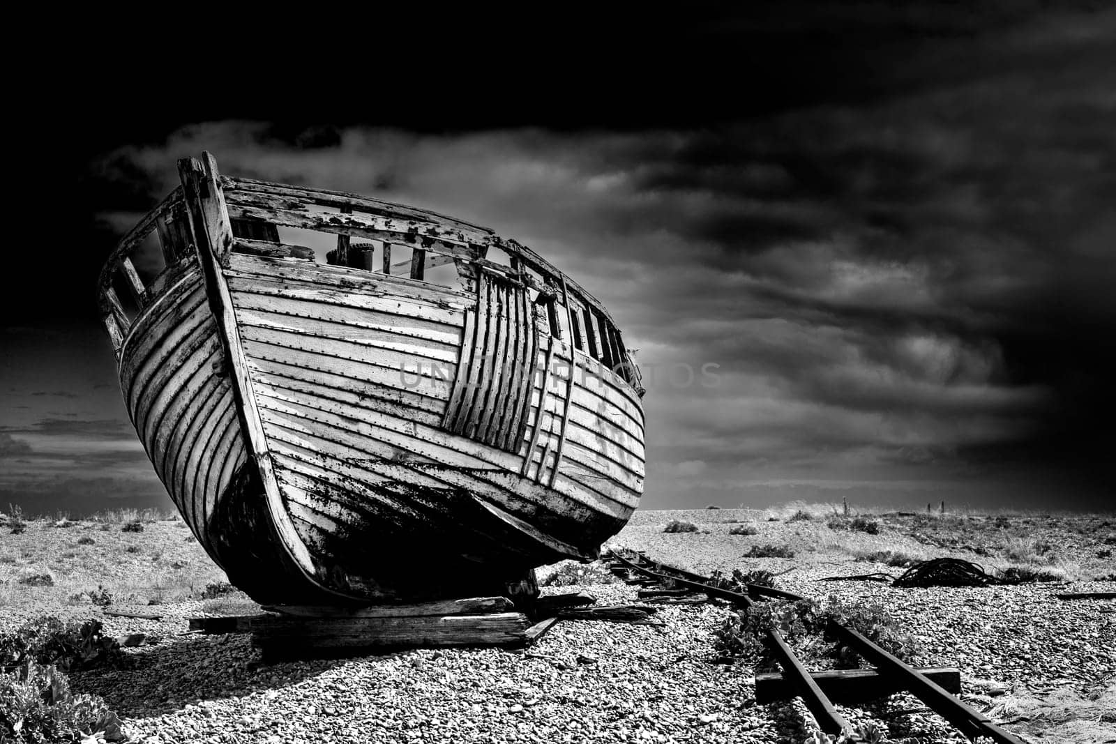 An old abandoned fishing boat stranded on a beech in black and white.
