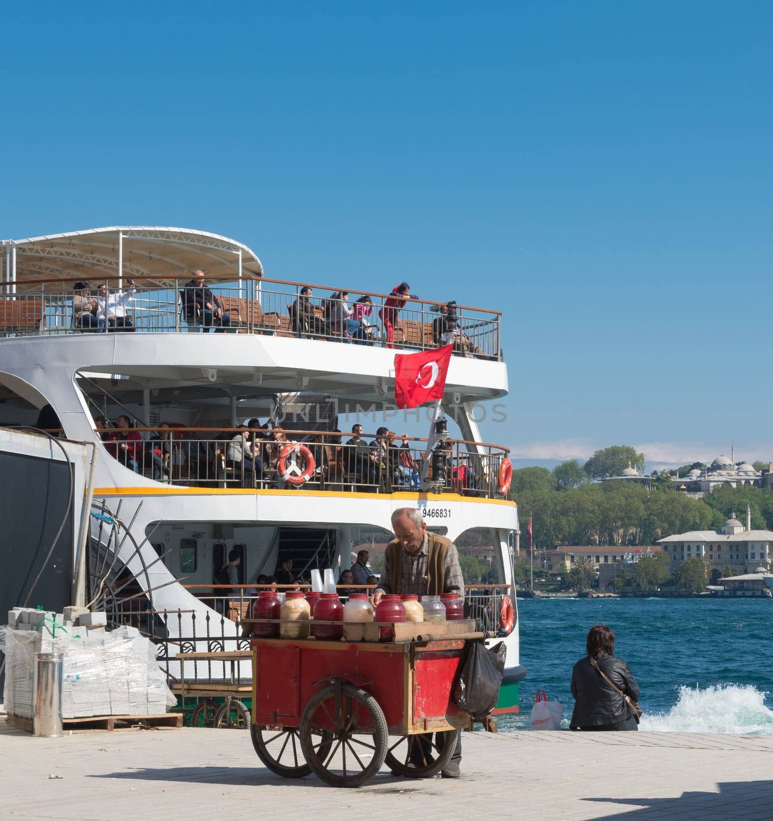 Old man selling drinks and foods on the karakoy pier in Istanbul in front of a leaving ferry boat.Eating on the street is part of local life here