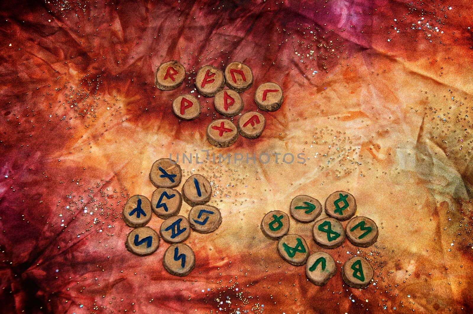 three sets of wooden runes, an ancient alphabet known as the futhark are on a colorful hand dyed fabric with small sparkling beads..Note