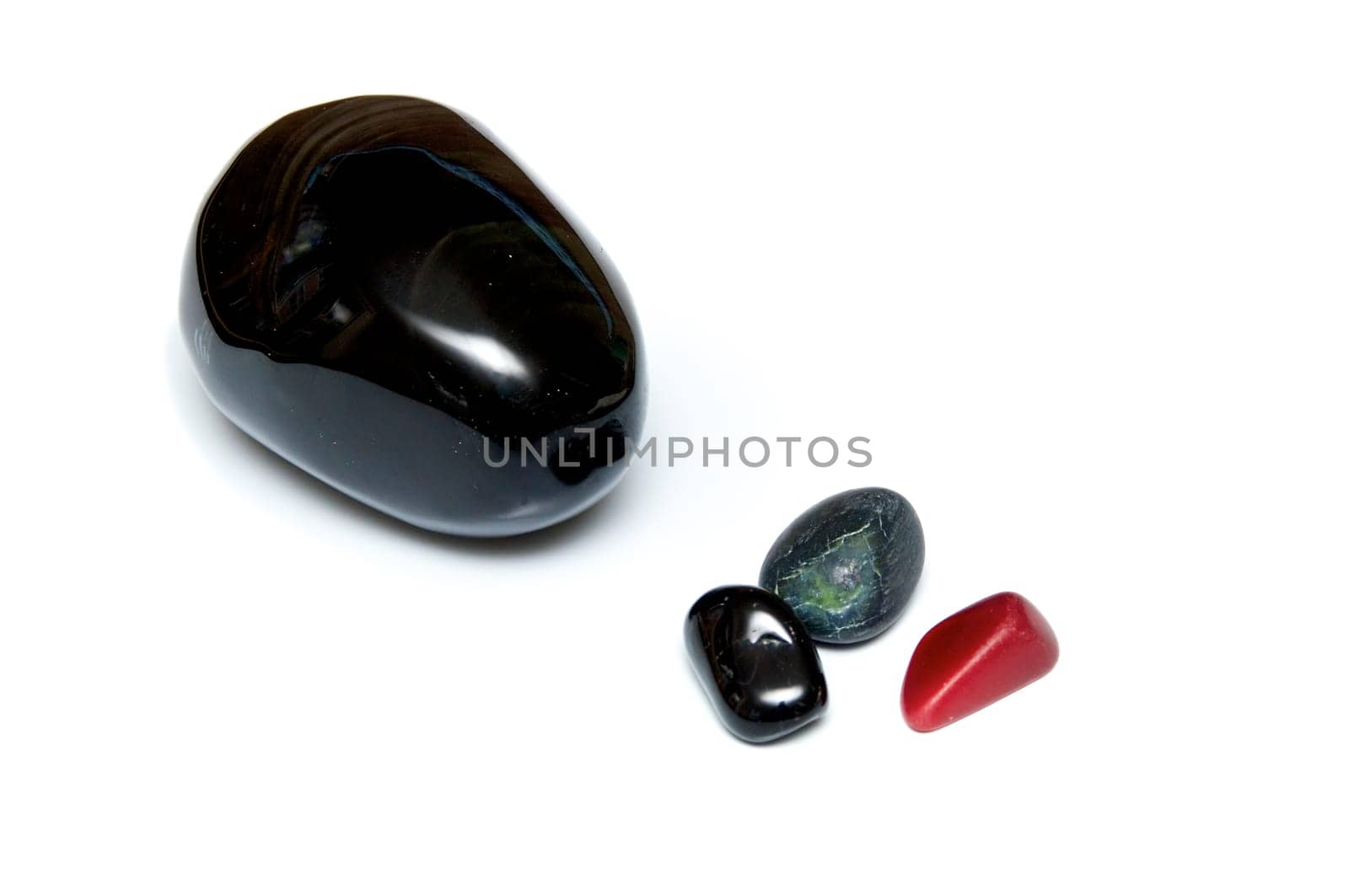 A collection of four smooth dark rocks used for massage over white. One large rock and three small.