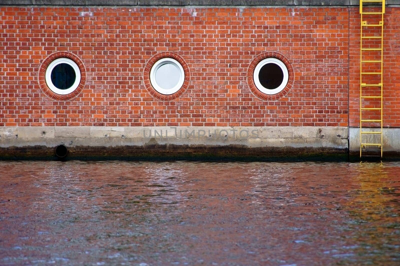 The photograph of a river boundary of bricks,with a ladder and round windows.