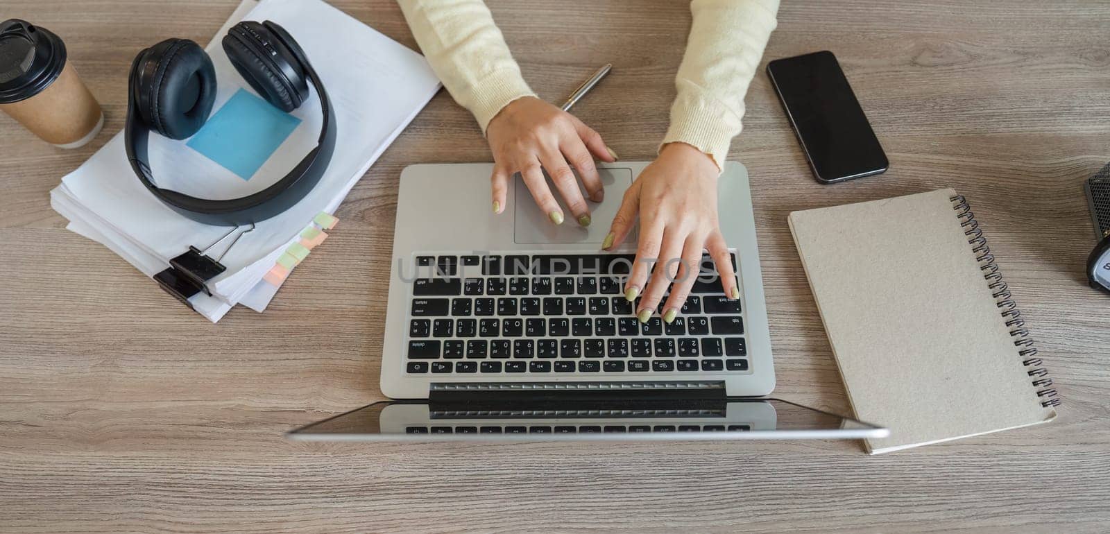 A focused view of hands typing on a laptop, with headphones and notes nearby, illustrating a productive home office environment.