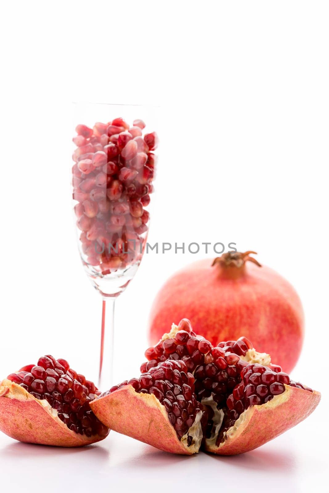 A pomegranate broken open, full of ripe, red seeds. Pomegranate seeds in a long-stemmed glass and an entire Punica granatum..