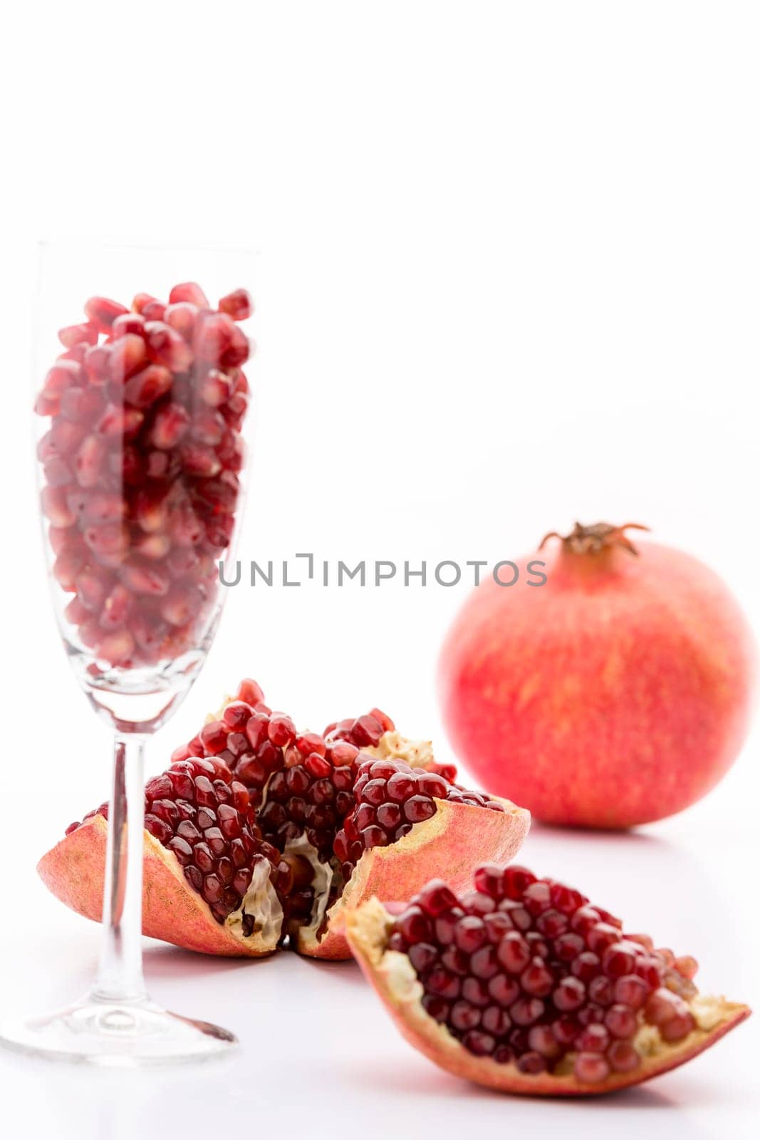 Red pomegranate seeds in a champagne glass and embedded in the reddish skin of the broken-up grenadine fruit. Behind is an entire Punica granatum..