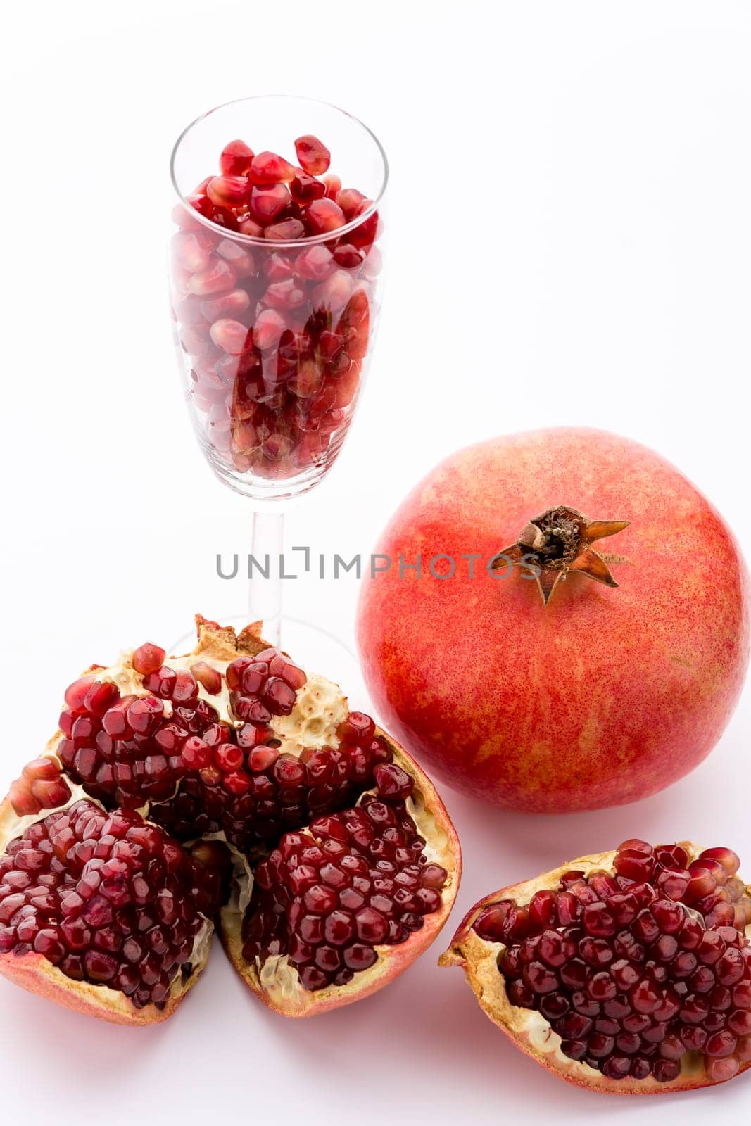 One whole pomegranate, Punica granatum. Next to it are pieces of a broken-up pomegranate. A champagne glass filled with ripe pomegranate seeds..