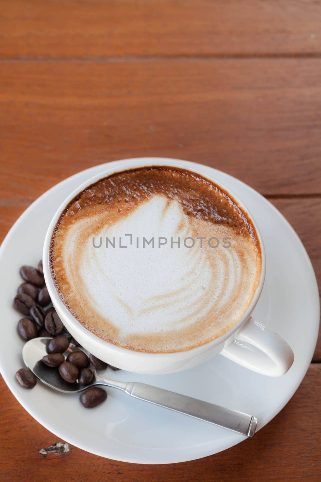 Cup of hot caffe latte with coffee grains on the wooden table