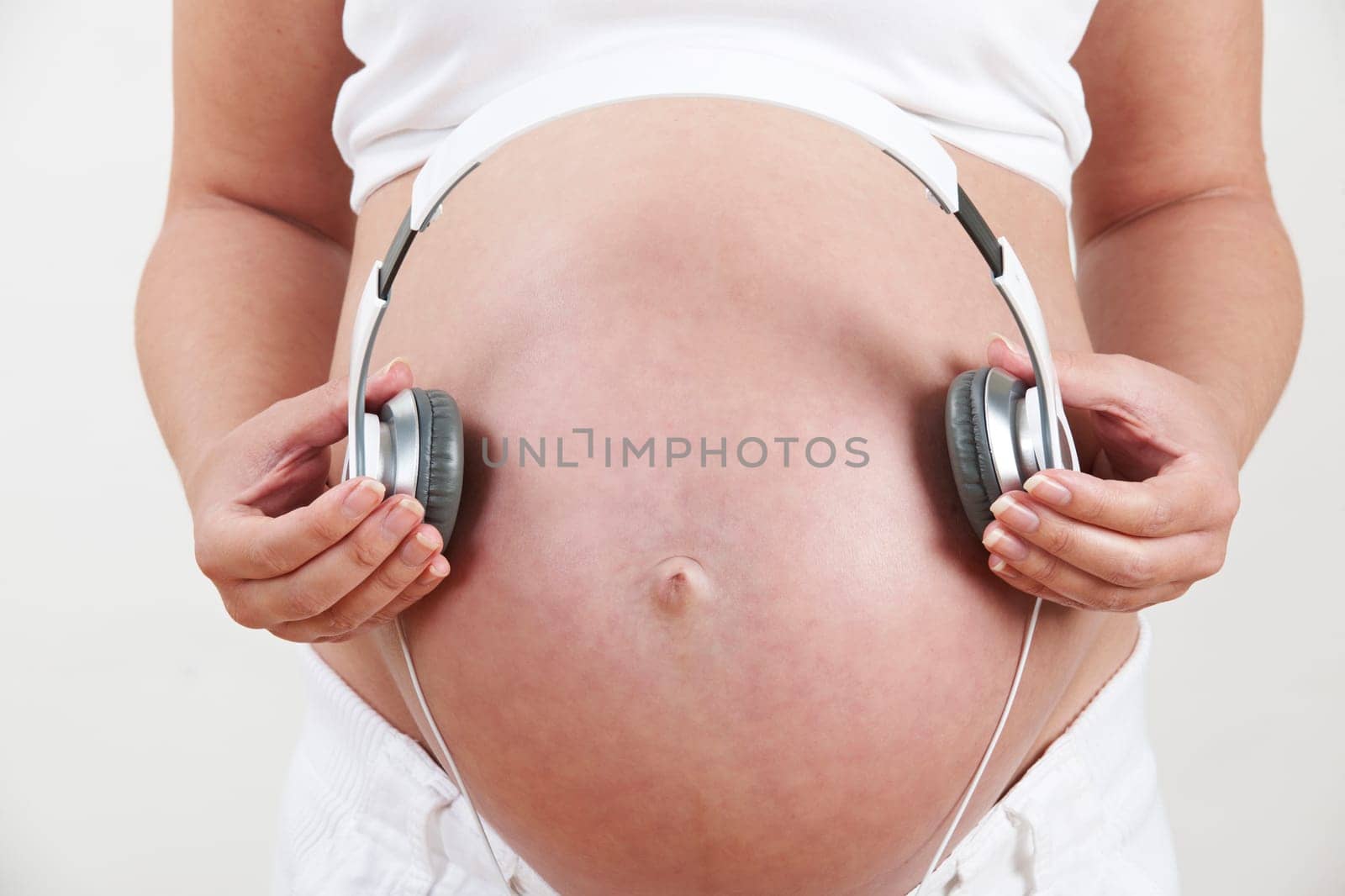 Close Up Of Pregnant Woman Holding Headphones Over Belly
