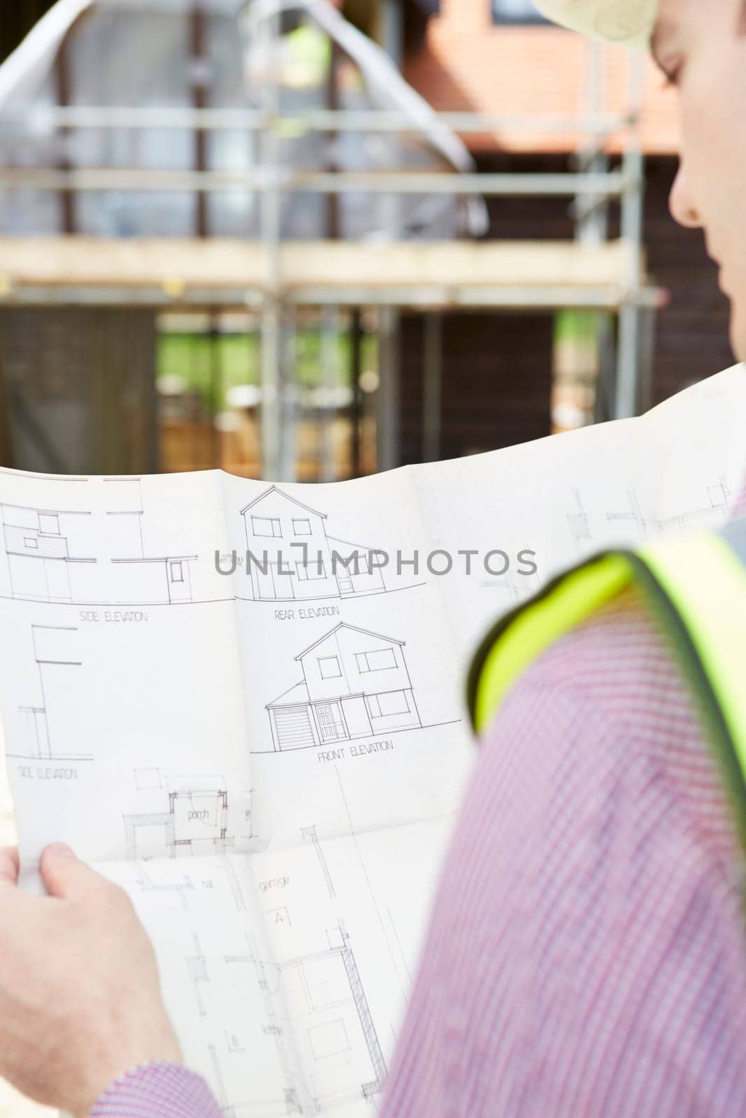 Architect On Building Site Looking At Plans For House