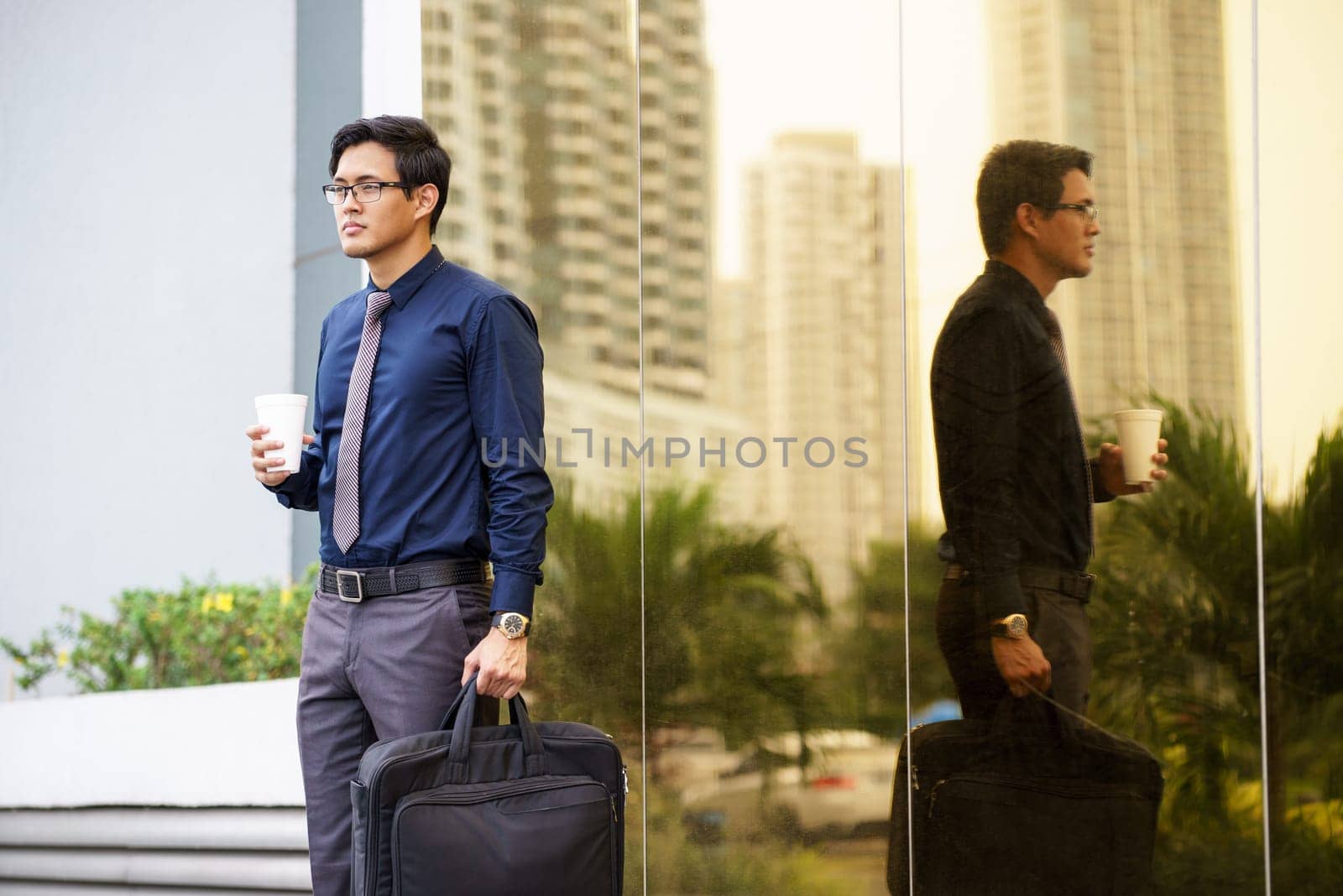 Portrait of chinese businessman standing near office building in Panama coffee cup and suitcase