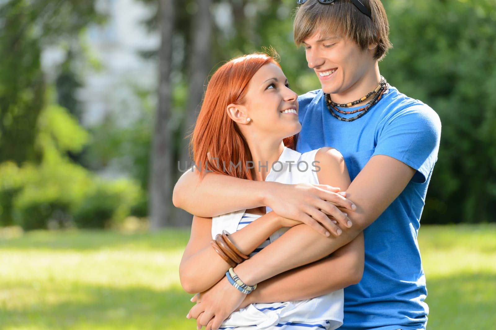 Smiling couple embracing looking at each other in sunny park