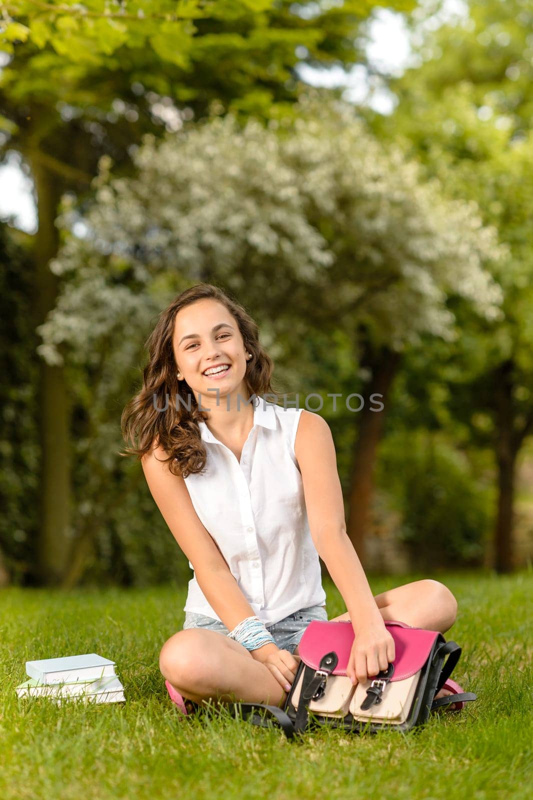 Happy student girl sitting on grass open school bag summer