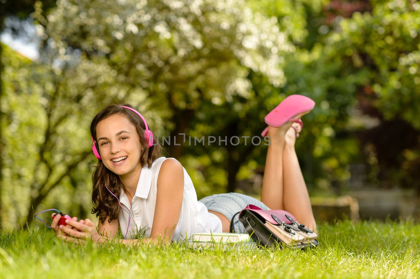 Laughing student girl with headphones lying grass listen music summer
