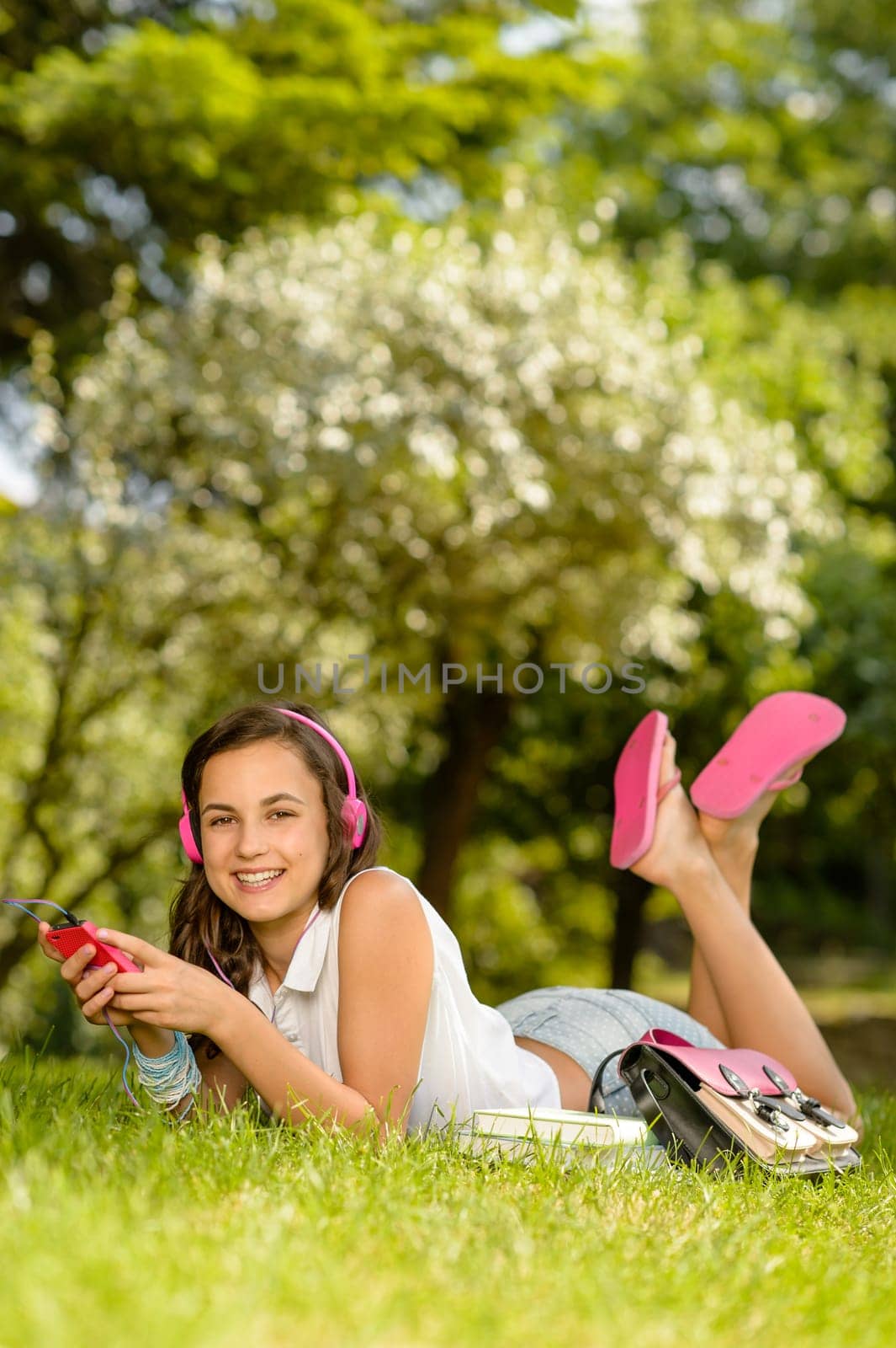 Smiling student girl lying in summer park listen to music