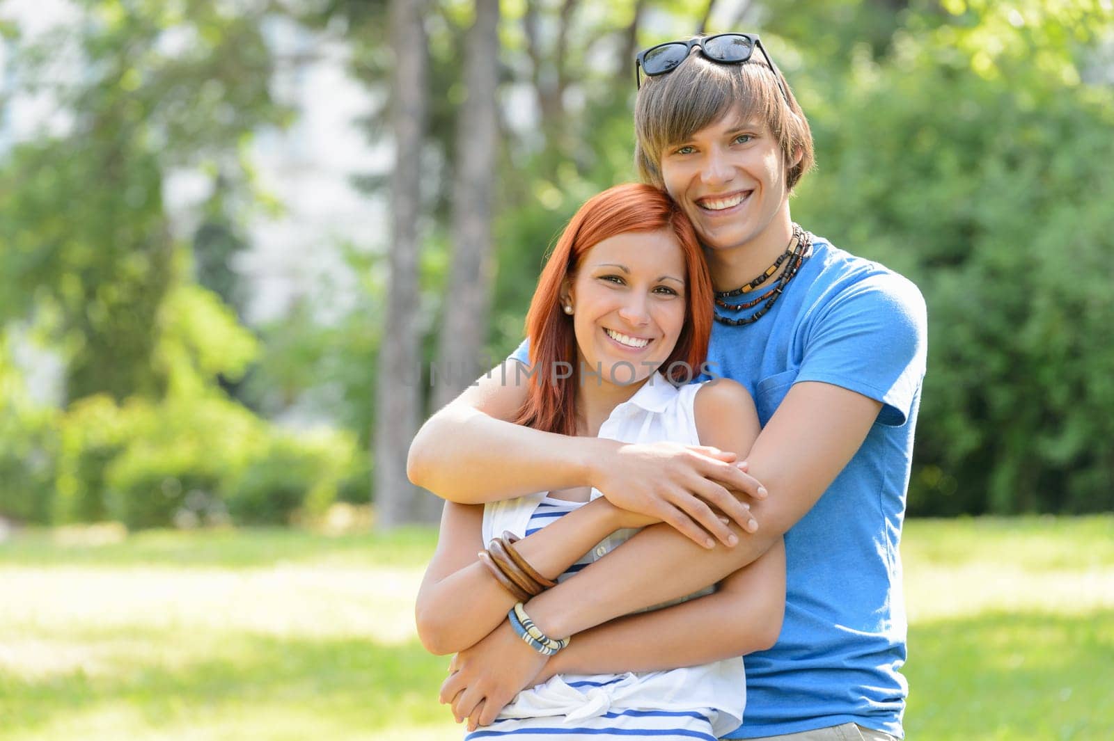 Teenage couple hugging in sunny park smiling at camera