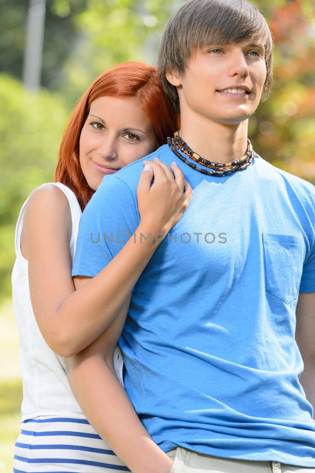Teenage girlfriend hugging her boyfriend from behind sunny park