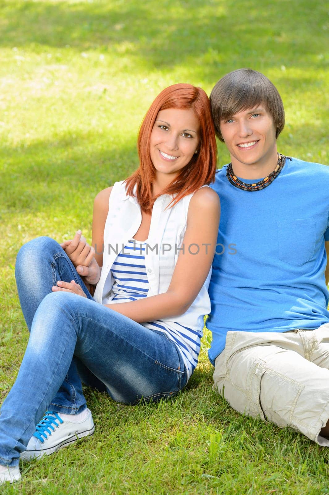 Teenage couple sitting on grass embracing in sunny park