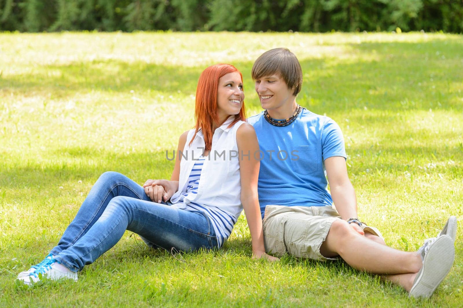 Teenage couple sitting on grass looking at each other summer