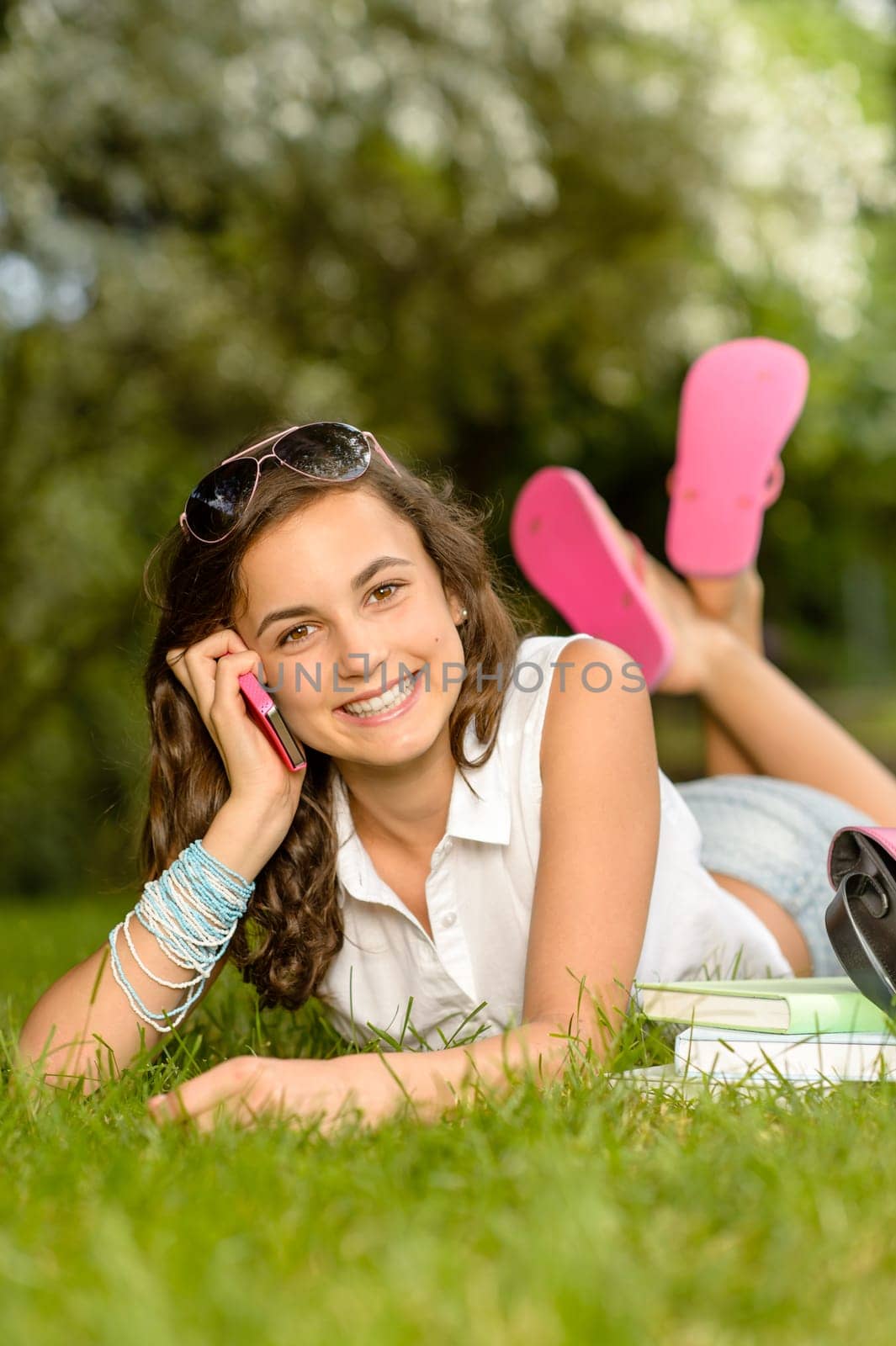 Cheerful student girl lying on grass calling mobile phone summer