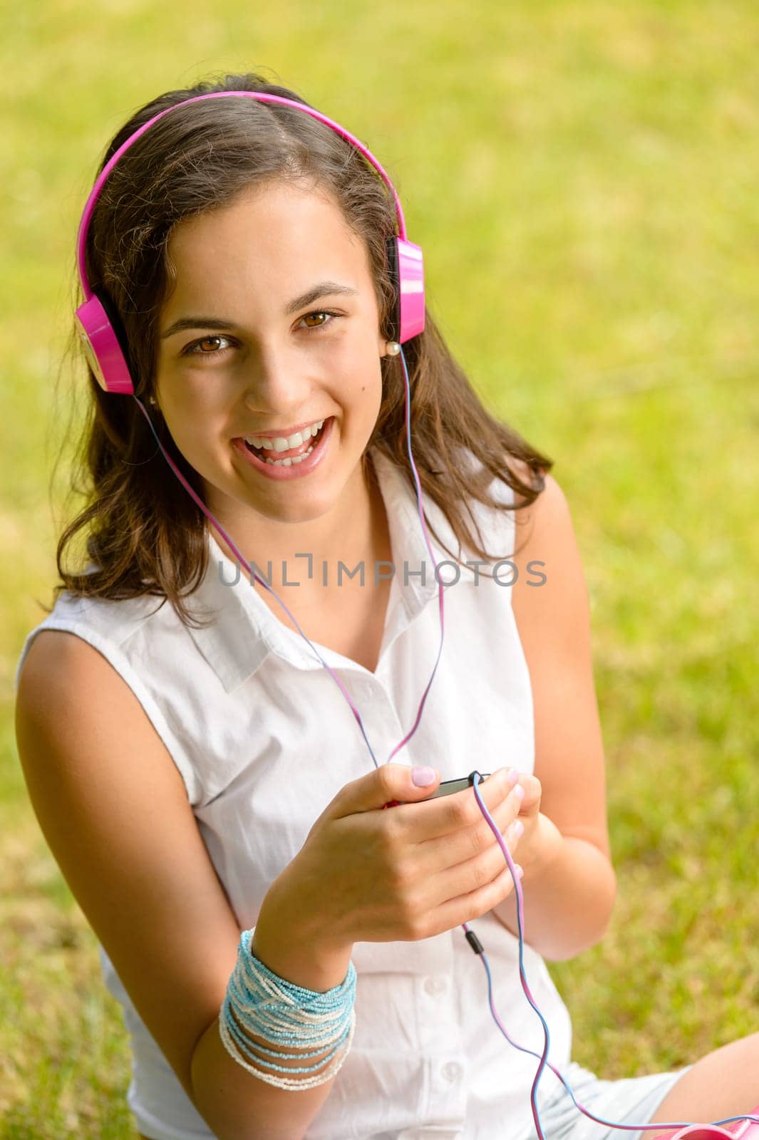 Laughing teenage girl listening to music sitting on grass summer