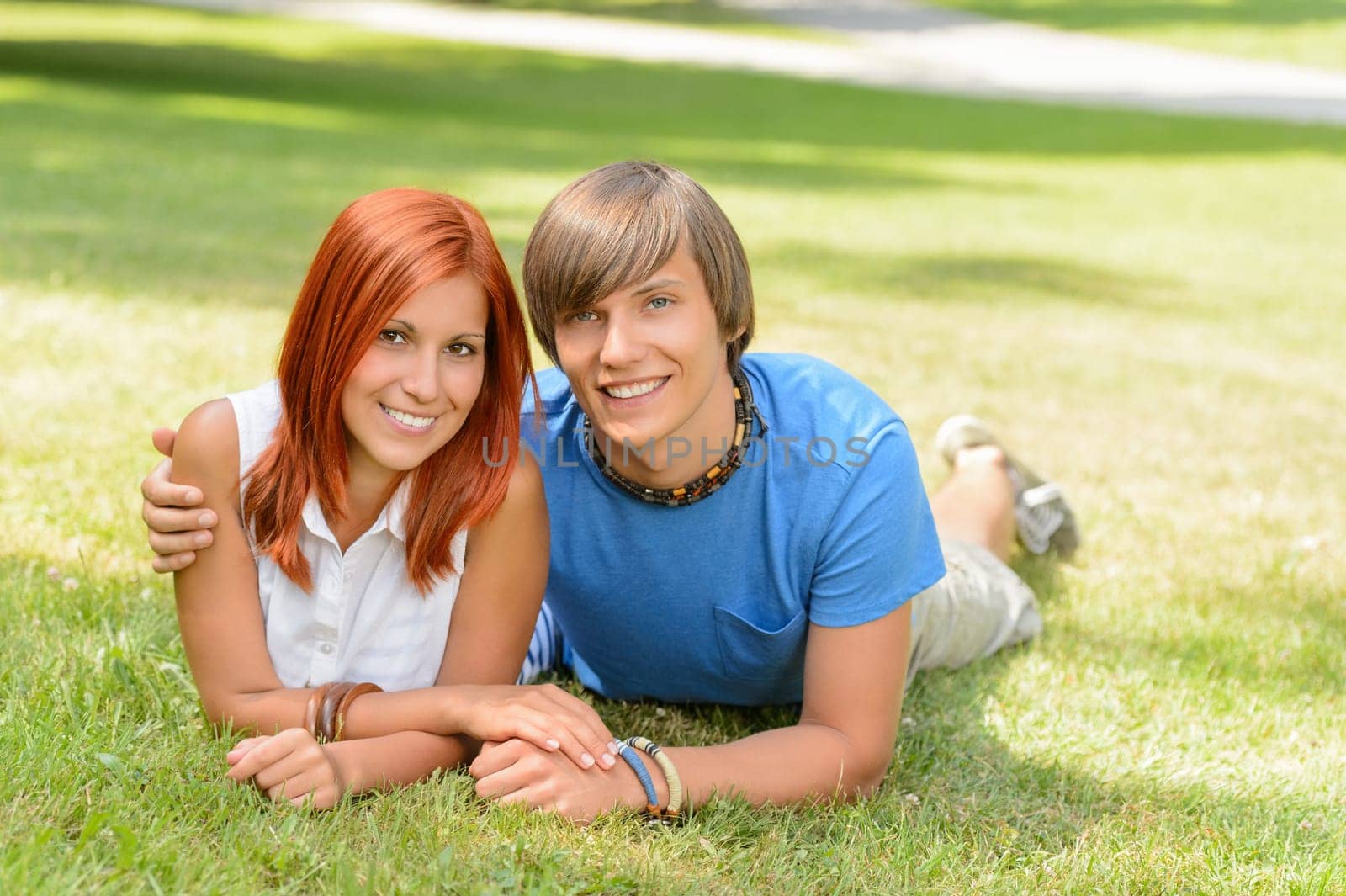 Teenage couple lying on grass summer love smiling at camera
