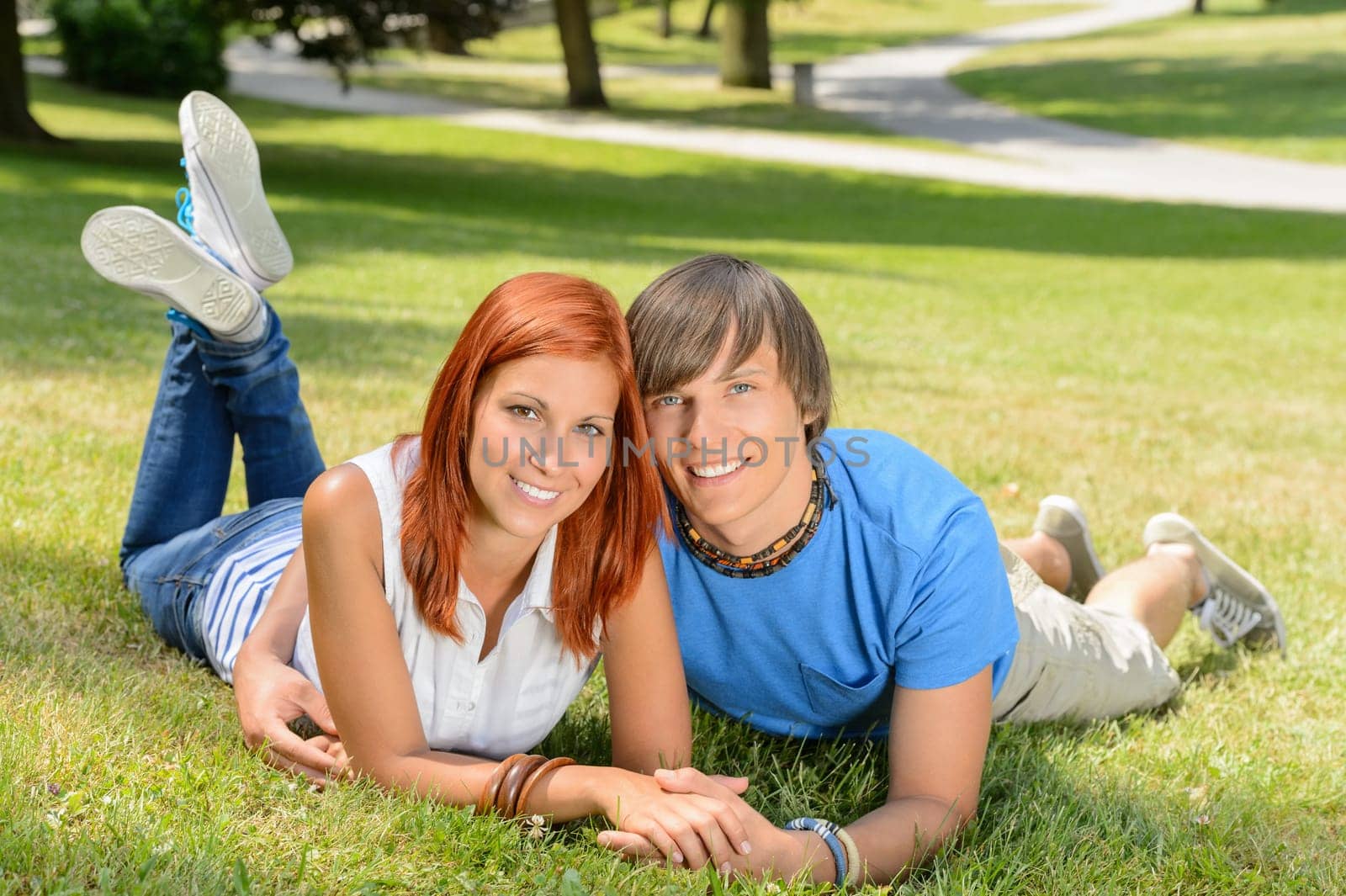 Smiling teenage couple lying in sunny park enjoy first love