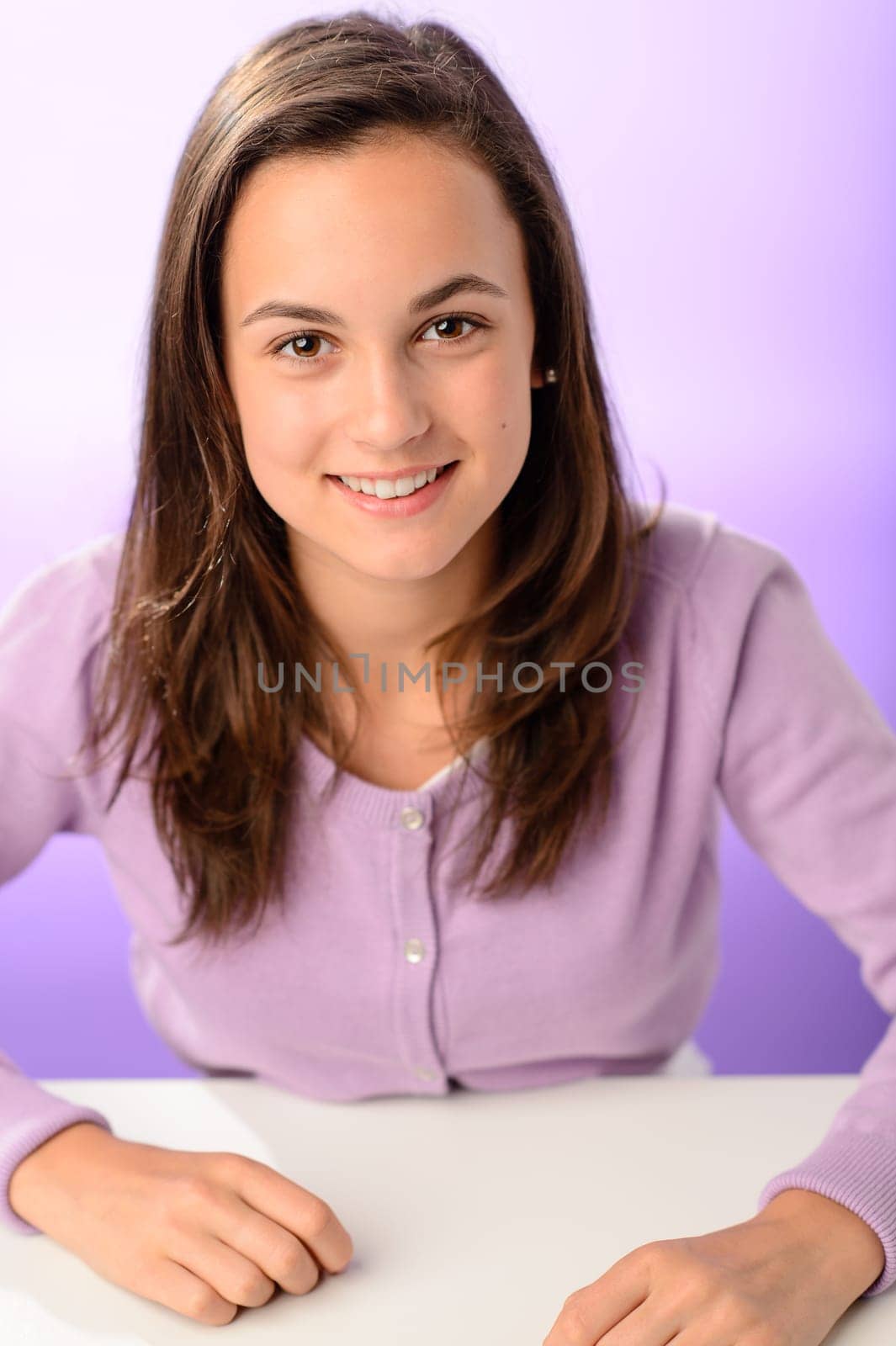 Happy student girl sitting behind desk on purple background portrait