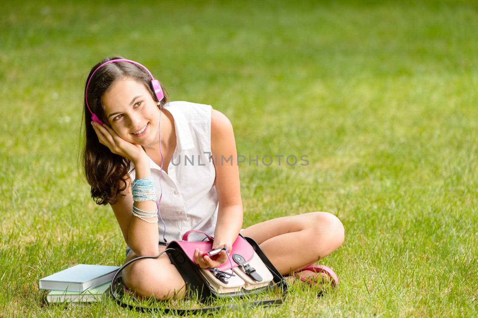 Student girl with pink headphones sitting on grass summer