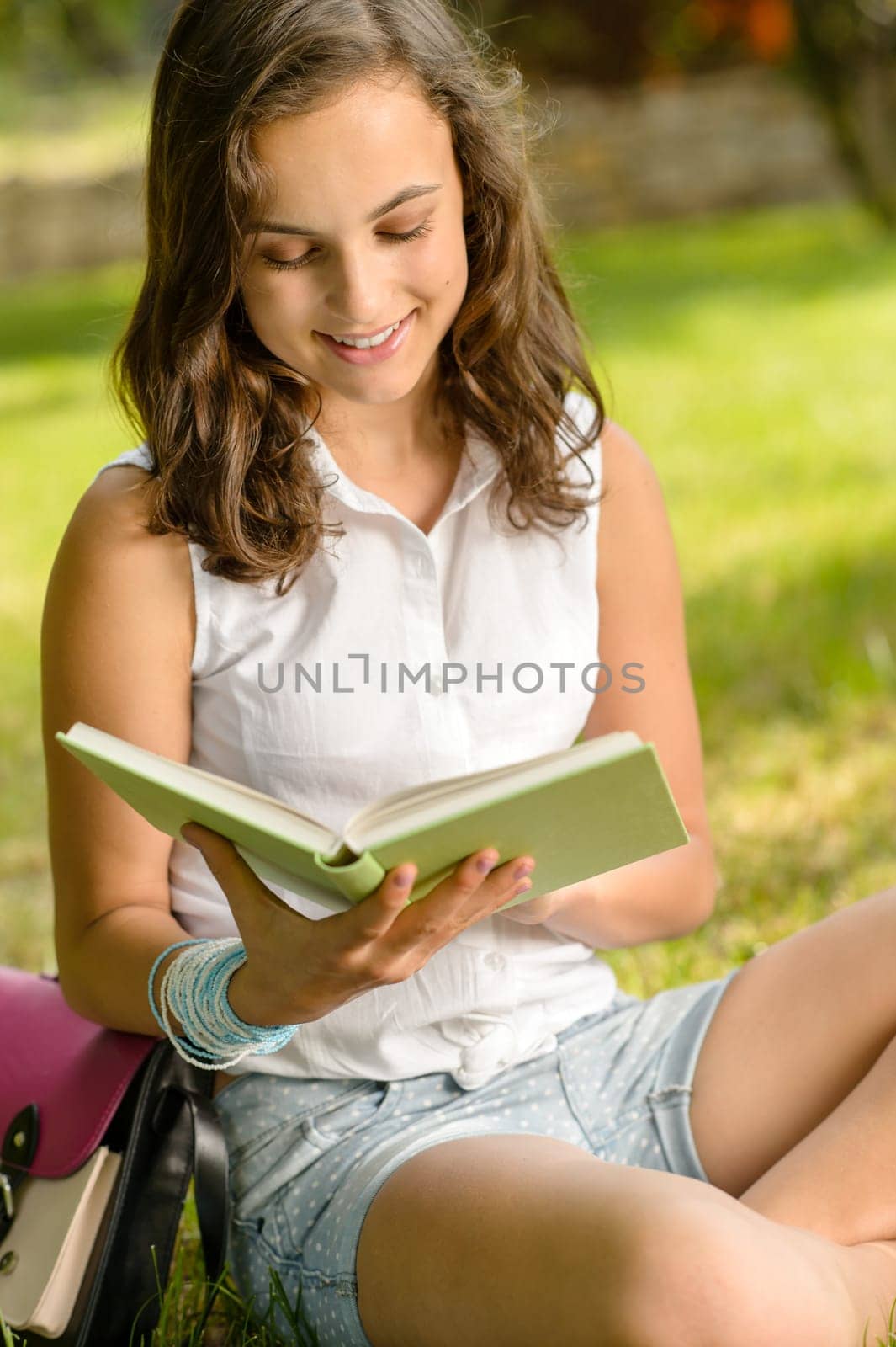 Smiling student girl reading book in park summer