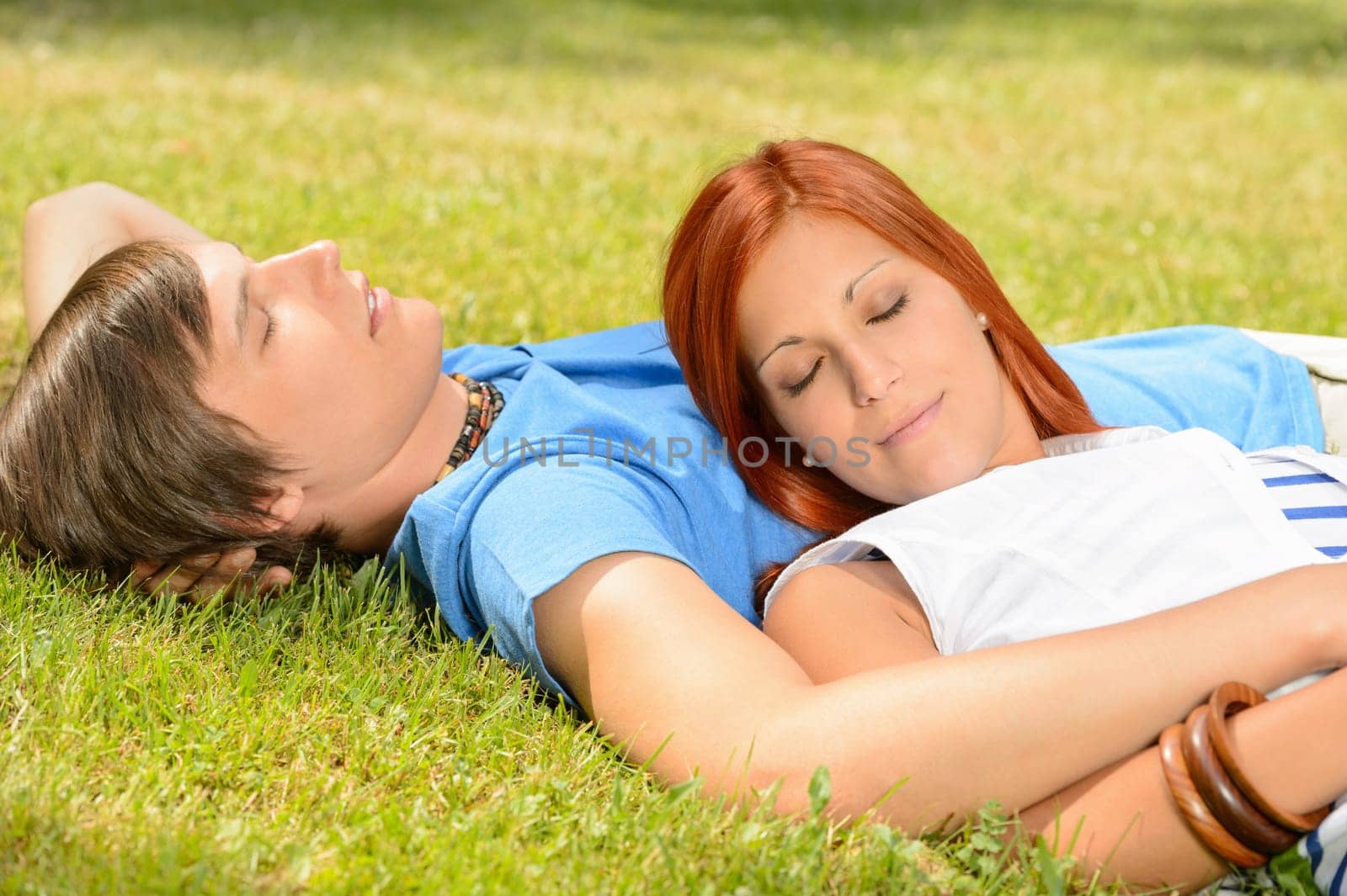 Teenage couple relaxing lying on grass closed eyes summer day