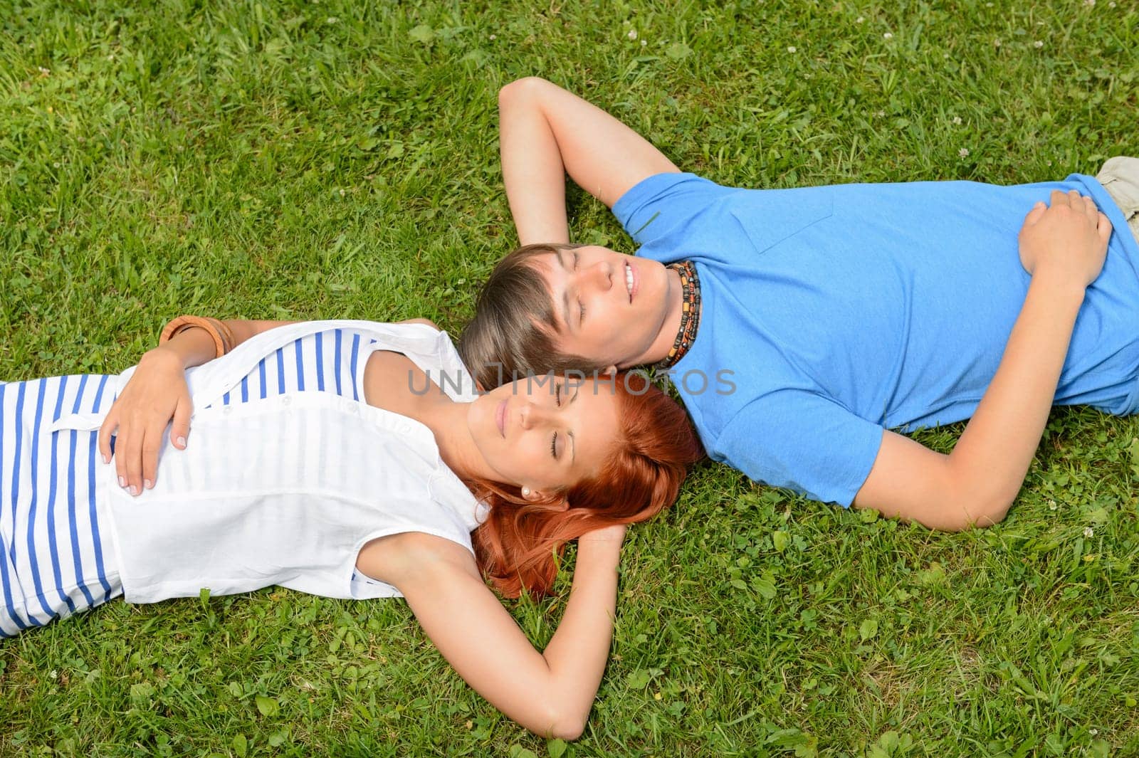 Teenage couple lying on grass relaxing closed eyes top view