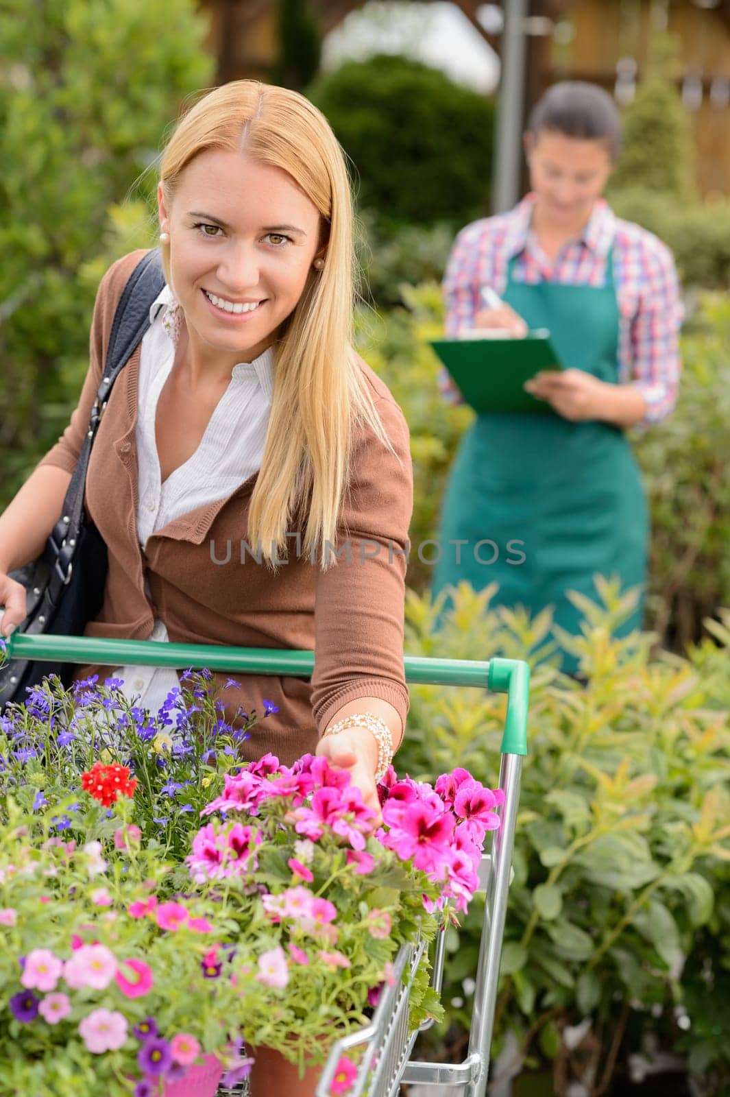 Smiling woman put flowers in shopping cart in garden center