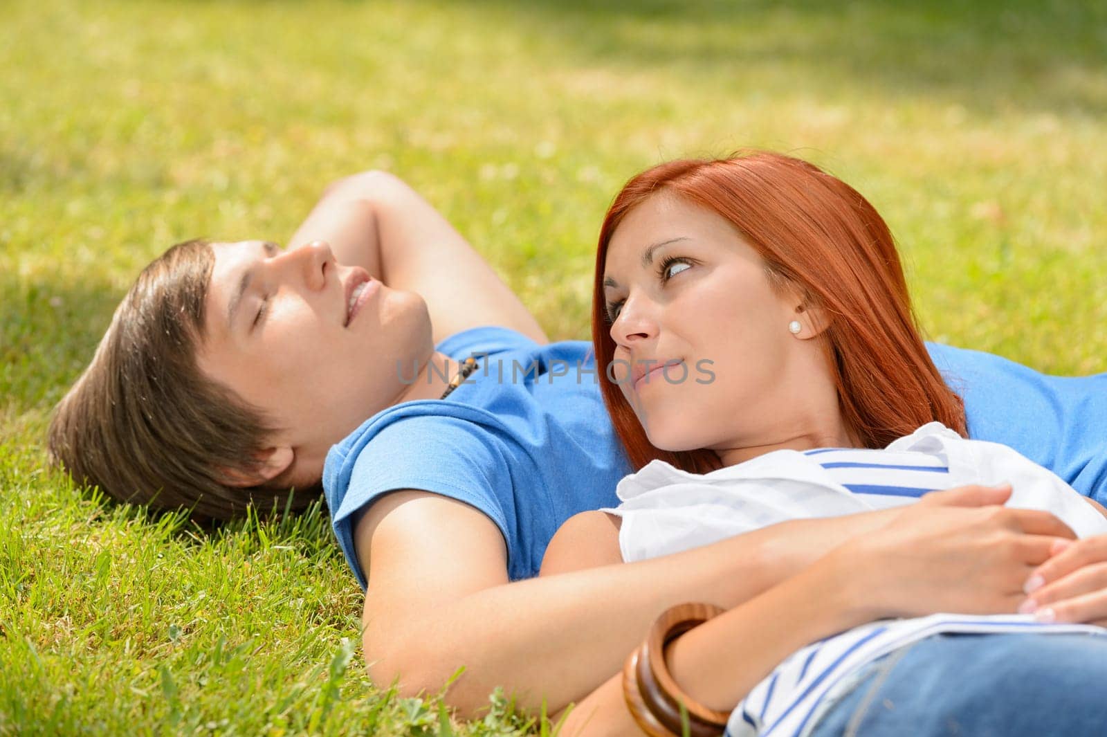 Teenage couple lying on grass summer girl looking at boyfriend