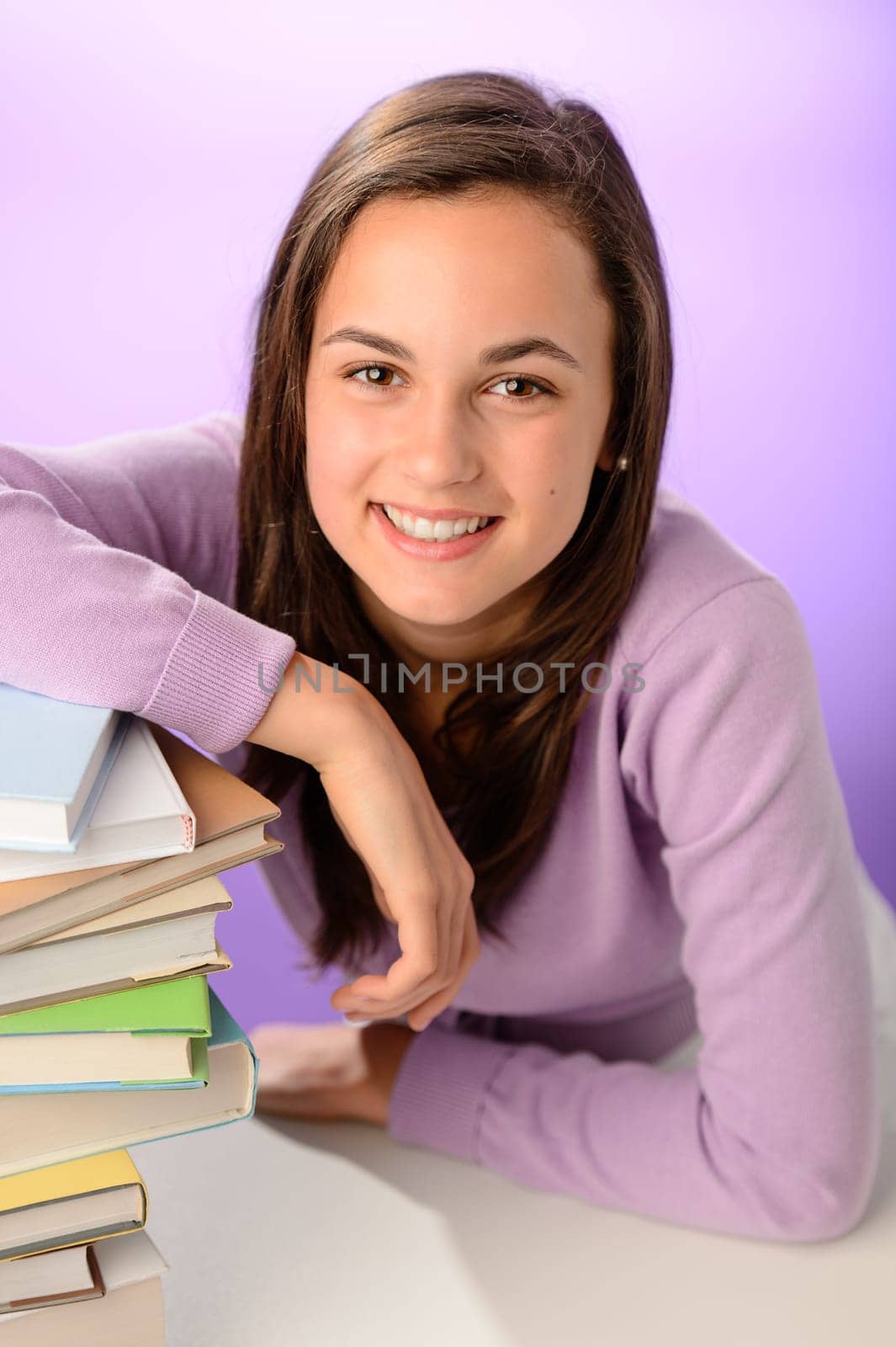 Smiling student girl with pile of books on purple background