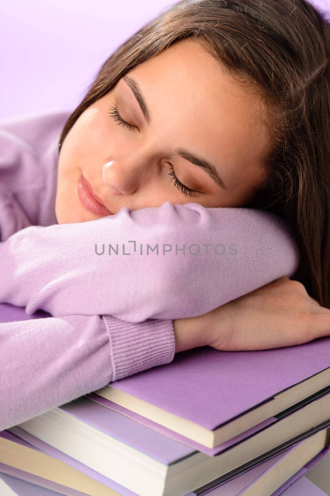 Tired student girl sleeping on stack of books purple background