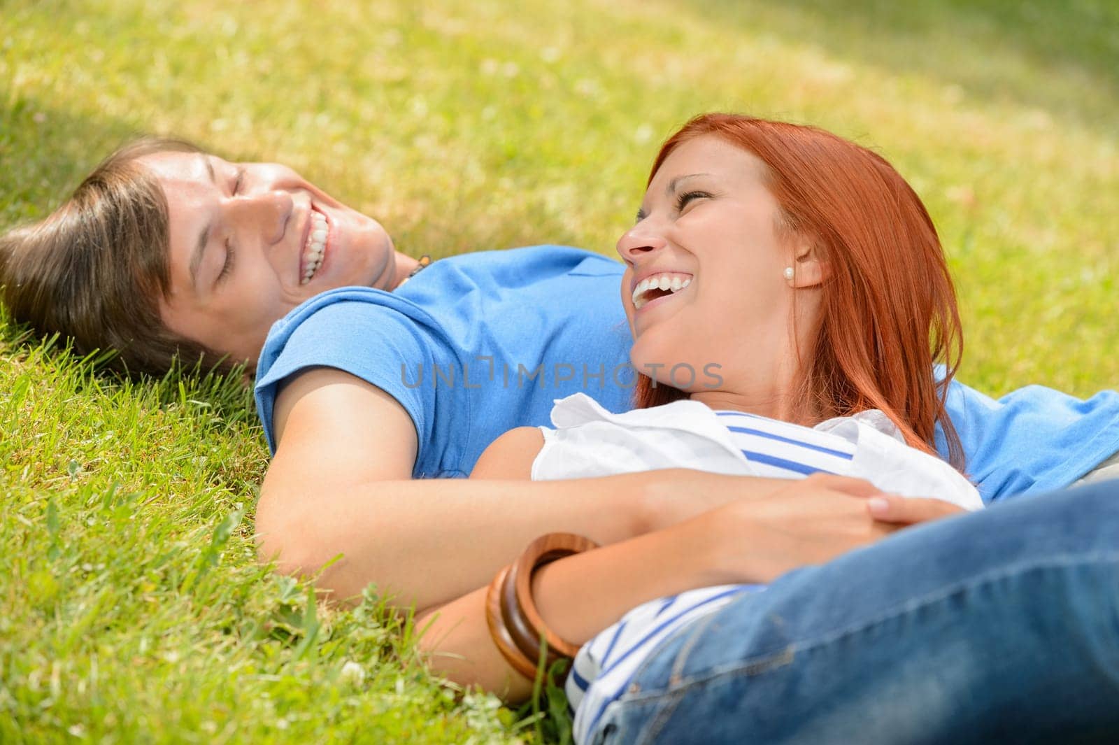 Cheerful teenage couple laughing at each other lying on grass
