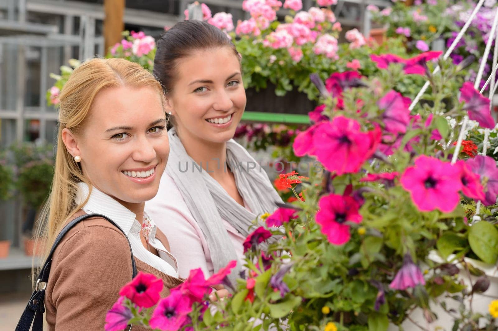 Two woman customers in garden center standing between colorful flowers