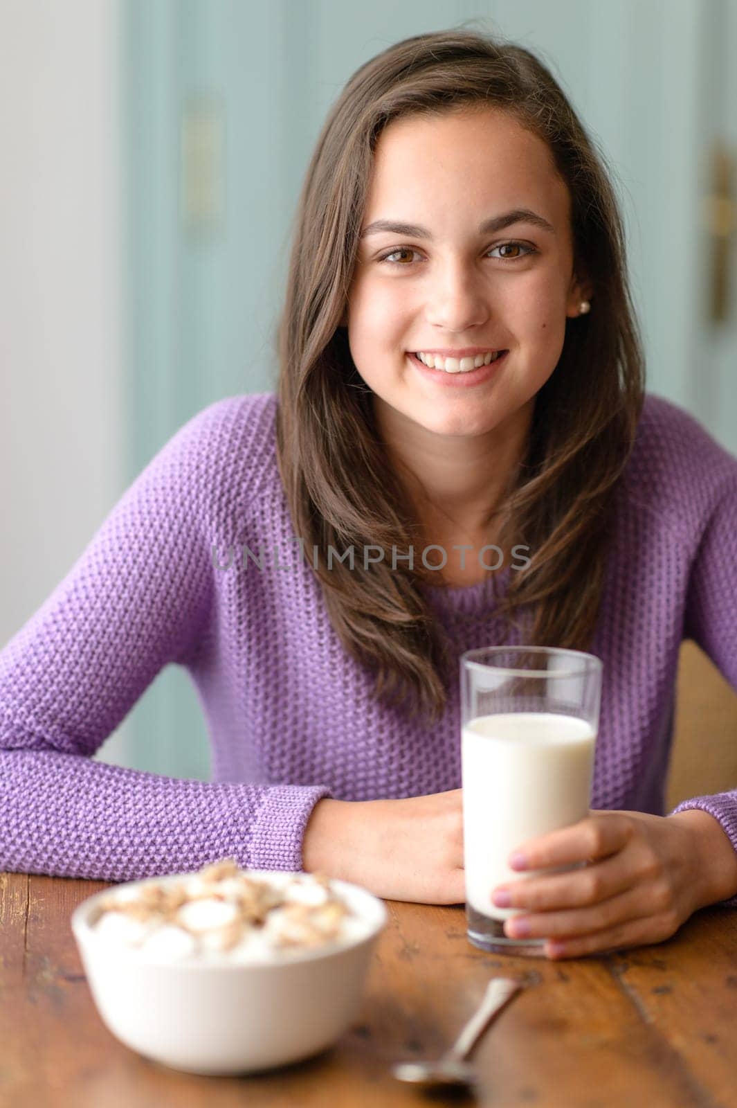 Smiling young woman holding glass of milk cereal breakfast table